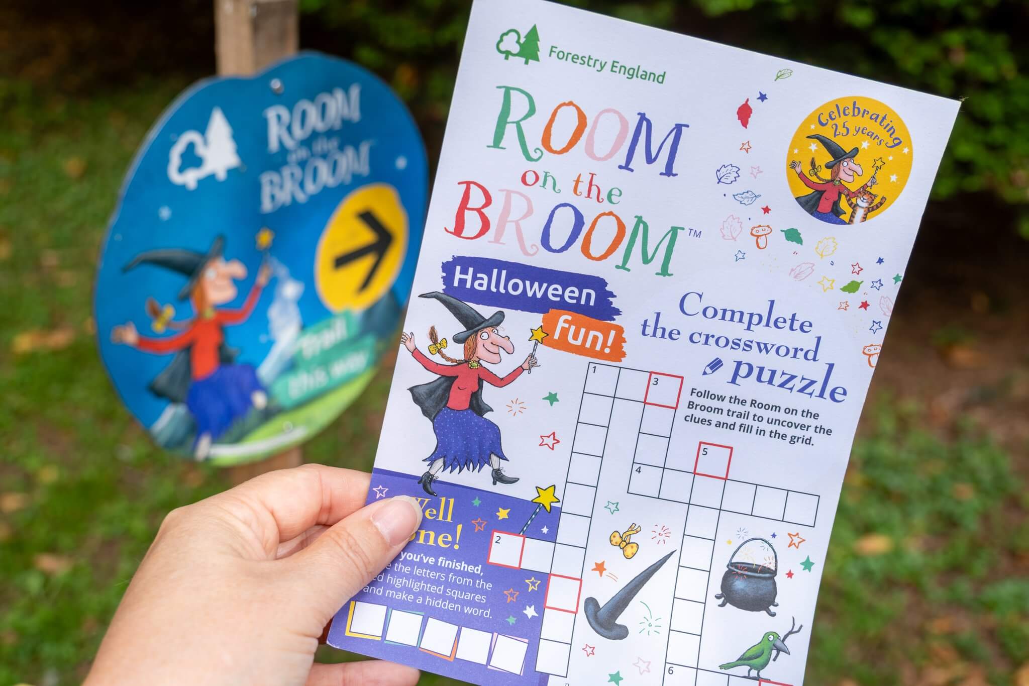 Room on the Broom Halloween crossword sheet held beside a trail waymarker