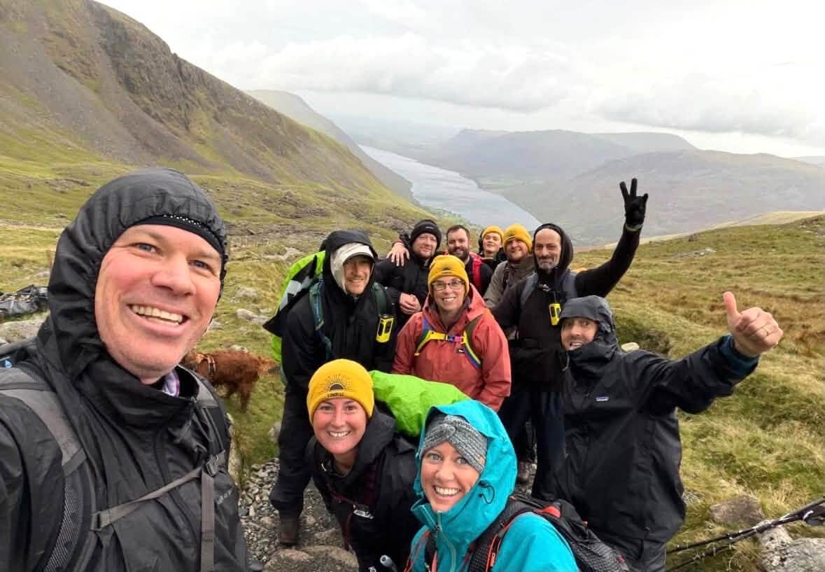 Team in waterproofs smiling on a mountain path above a lake