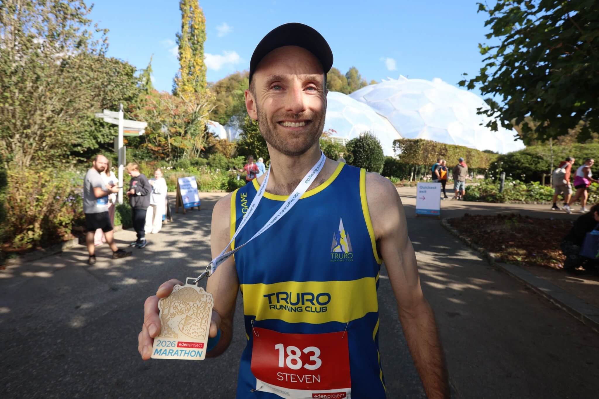 Steven Reynolds holding his medal in front of the Eden Project Biomes