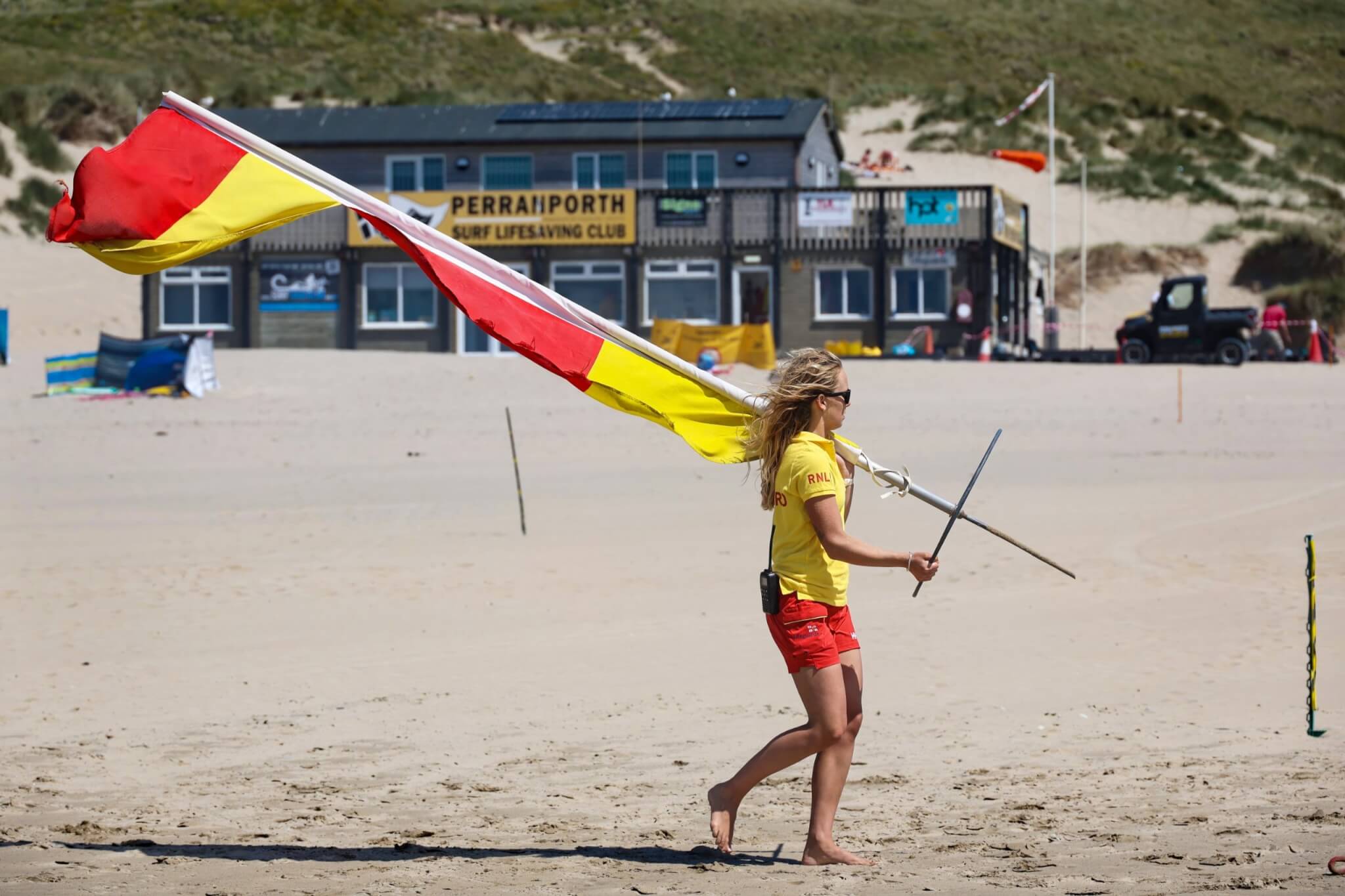 RNLI lifeguard carrying a red and yellow flag on Perranporth beach