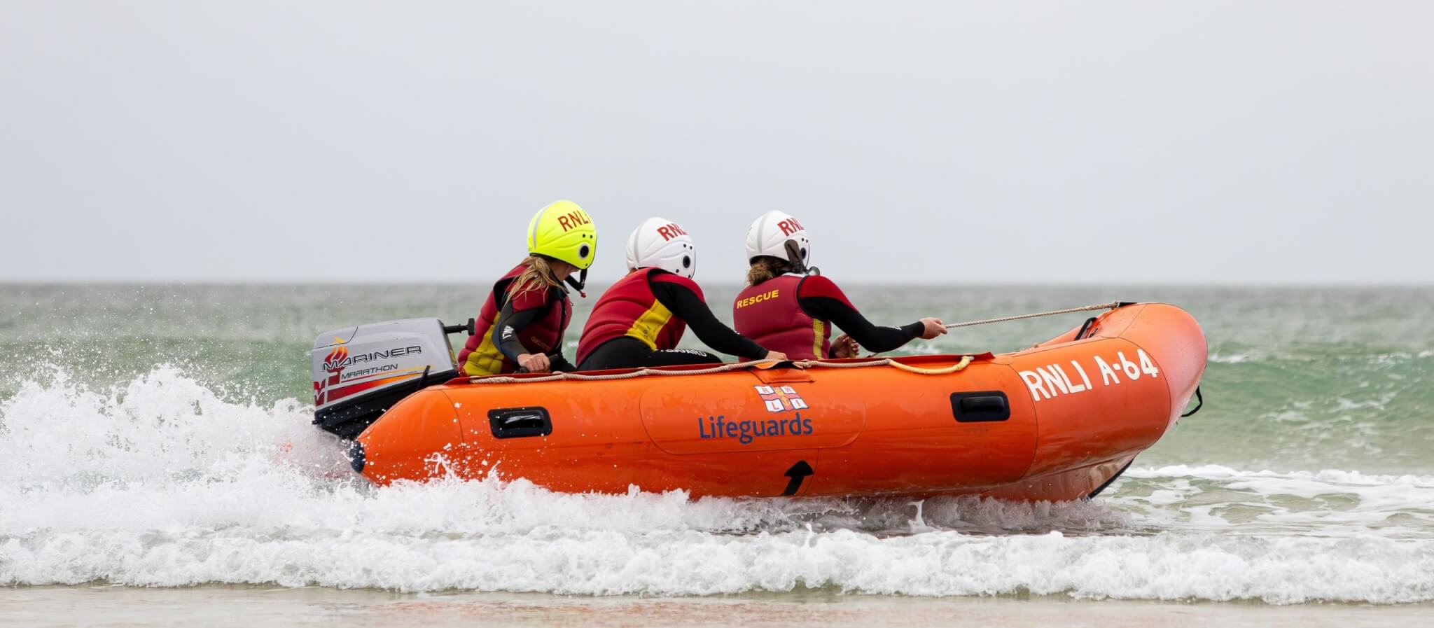 Three RNLI lifeguards on an inshore rescue boat at Fistral