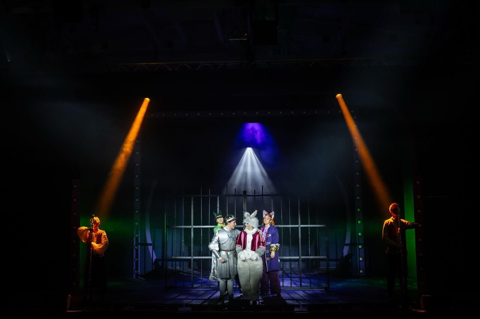BOOM Theatre cast on stage in Wonderland the Musical at Truro School, with a knight, White Rabbit and fox characters lit by spotlights