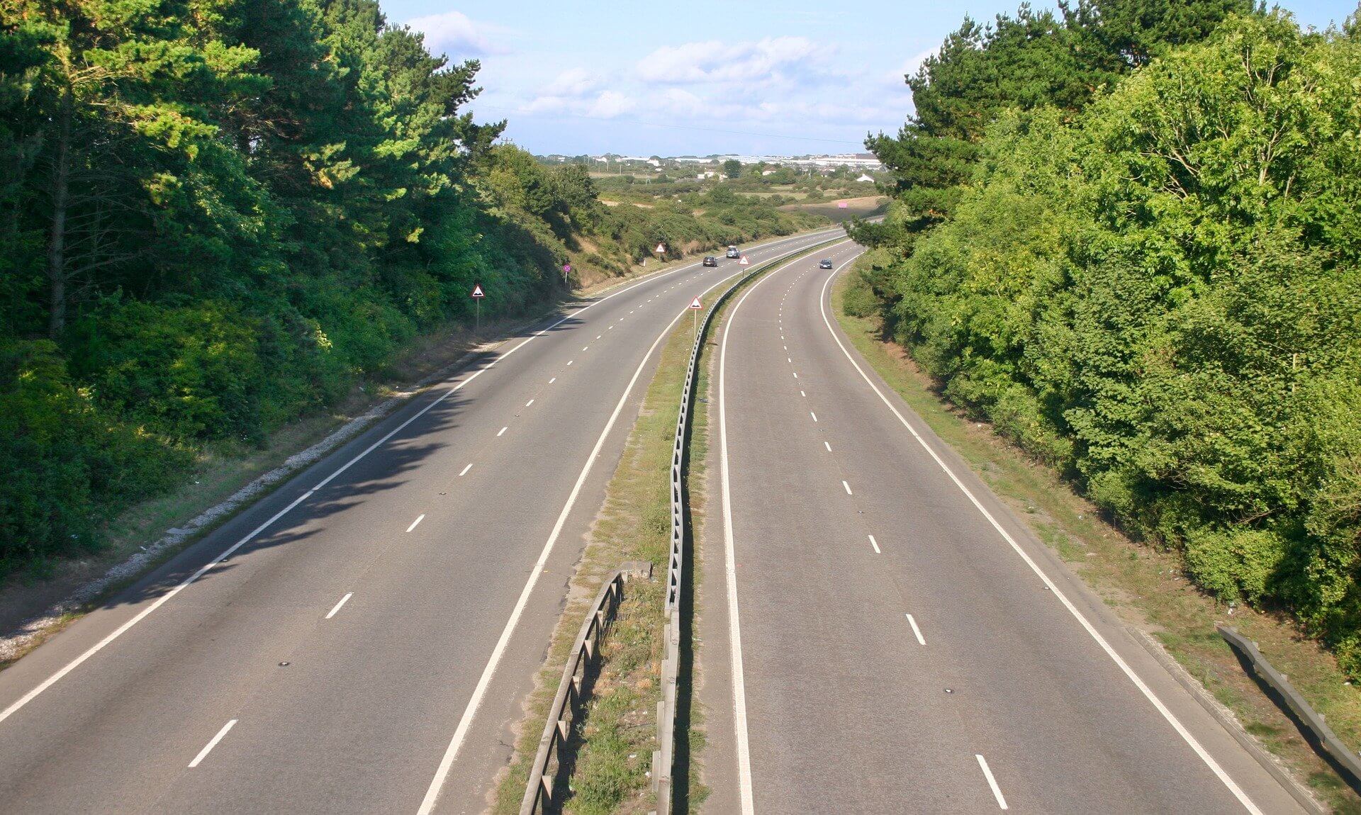 A dual carriageway seen from a bridge, with trees on both sides