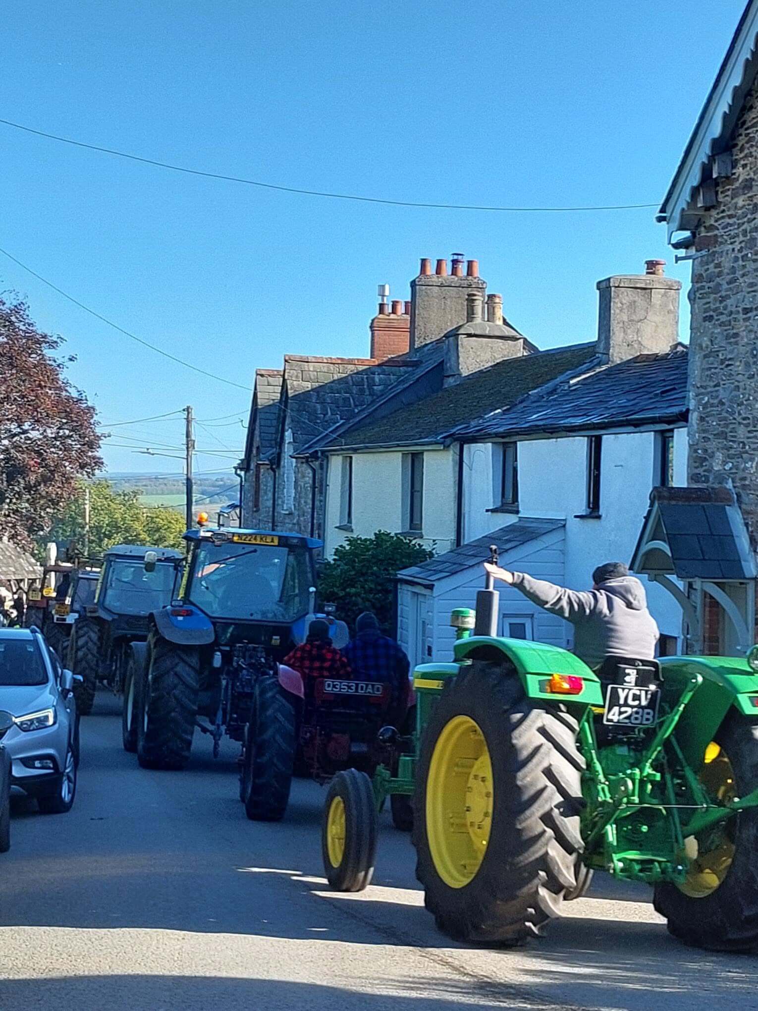 Tractors on the Bill Browning Memorial Tractor Run passing cottages near Lawhitton