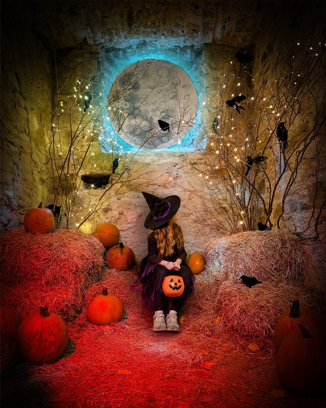 Child in a witch costume sitting among pumpkins and straw bales in a cell at Bodmin Jail