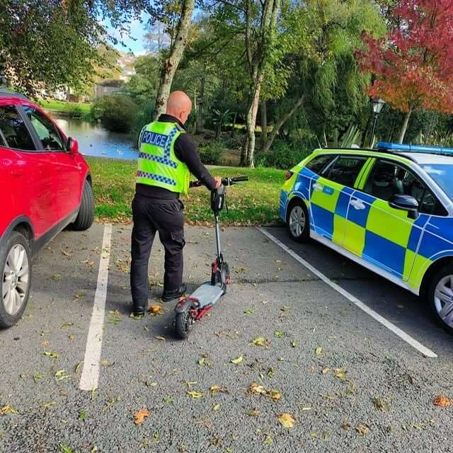 Police officer with a seized e-scooter beside a police car in Bodmin