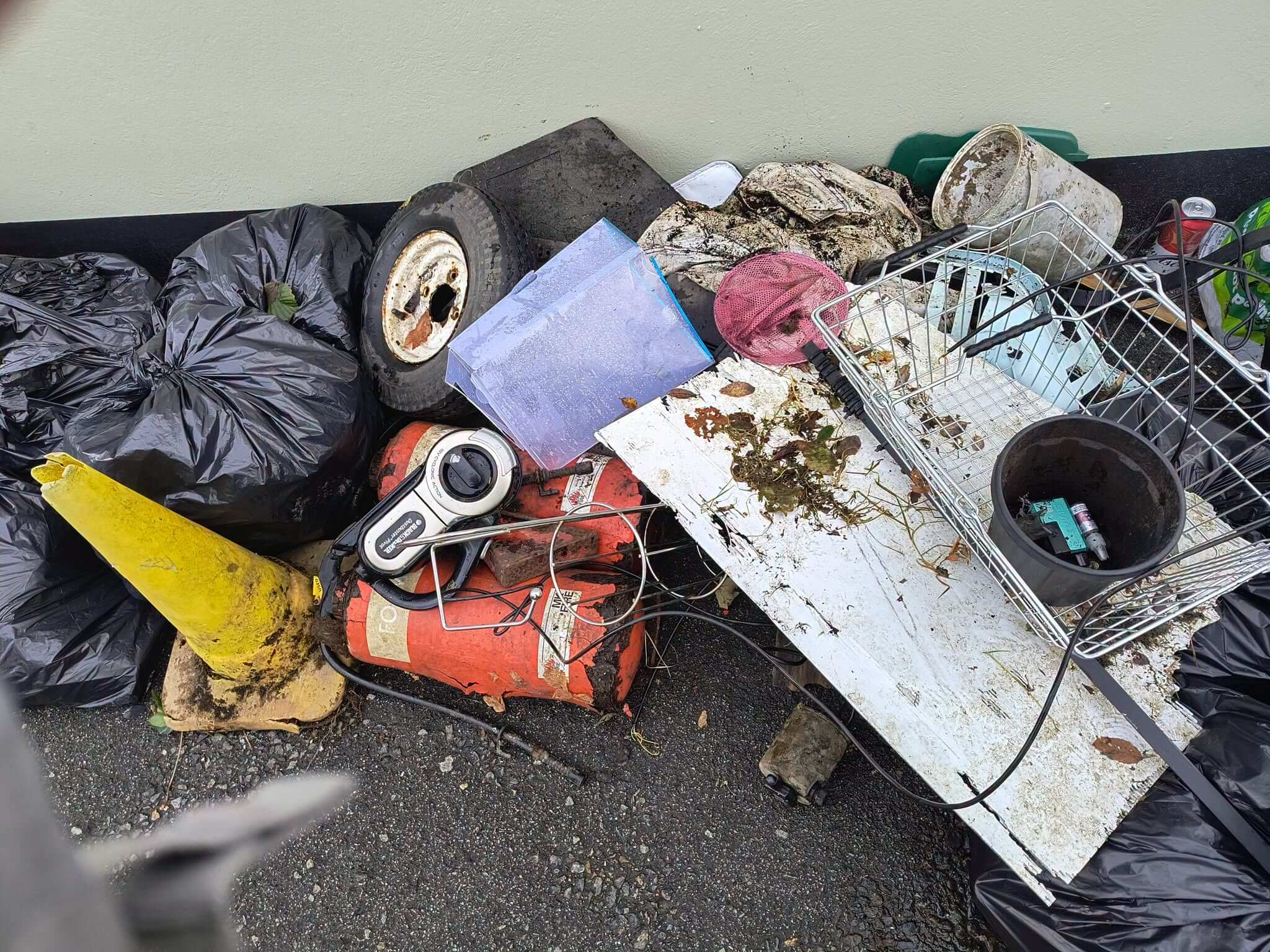 Pile of rubbish including bin bags, a tyre, traffic cone, fire extinguishers and a hoover