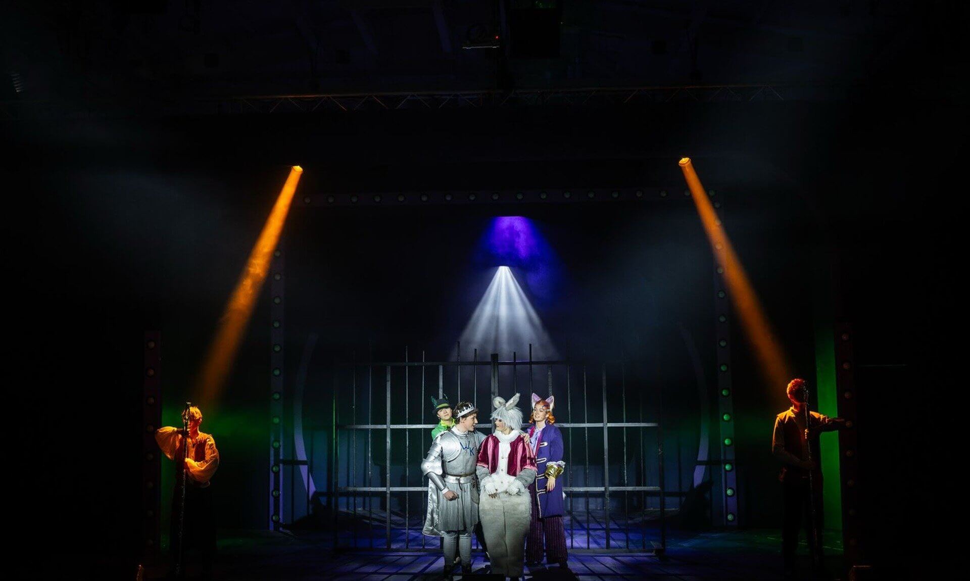 BOOM Theatre cast on stage in Wonderland the Musical at Truro School, with a knight, White Rabbit and fox characters lit by spotlights