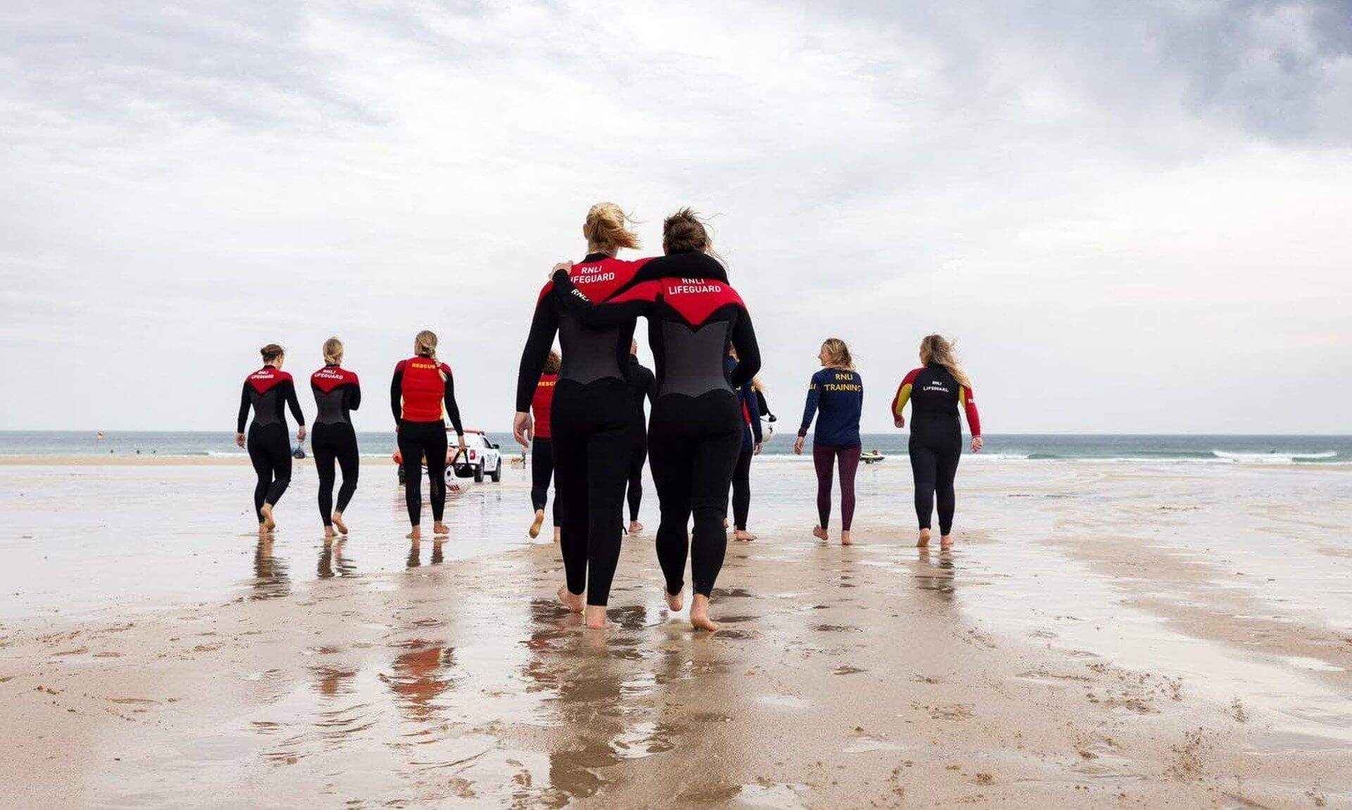 RNLI lifeguards in wetsuits walking down a wet beach towards the sea