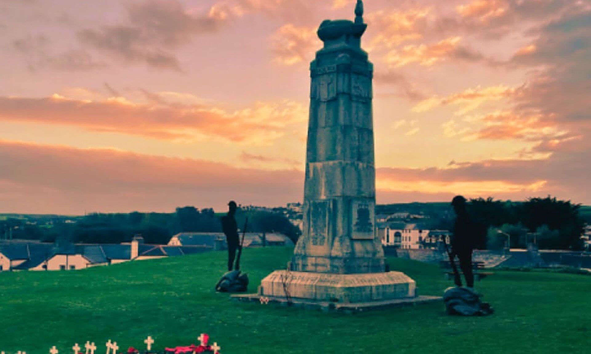 Bude War Memorial on Shalder Hill at sunset, with crosses and poppies on the grass