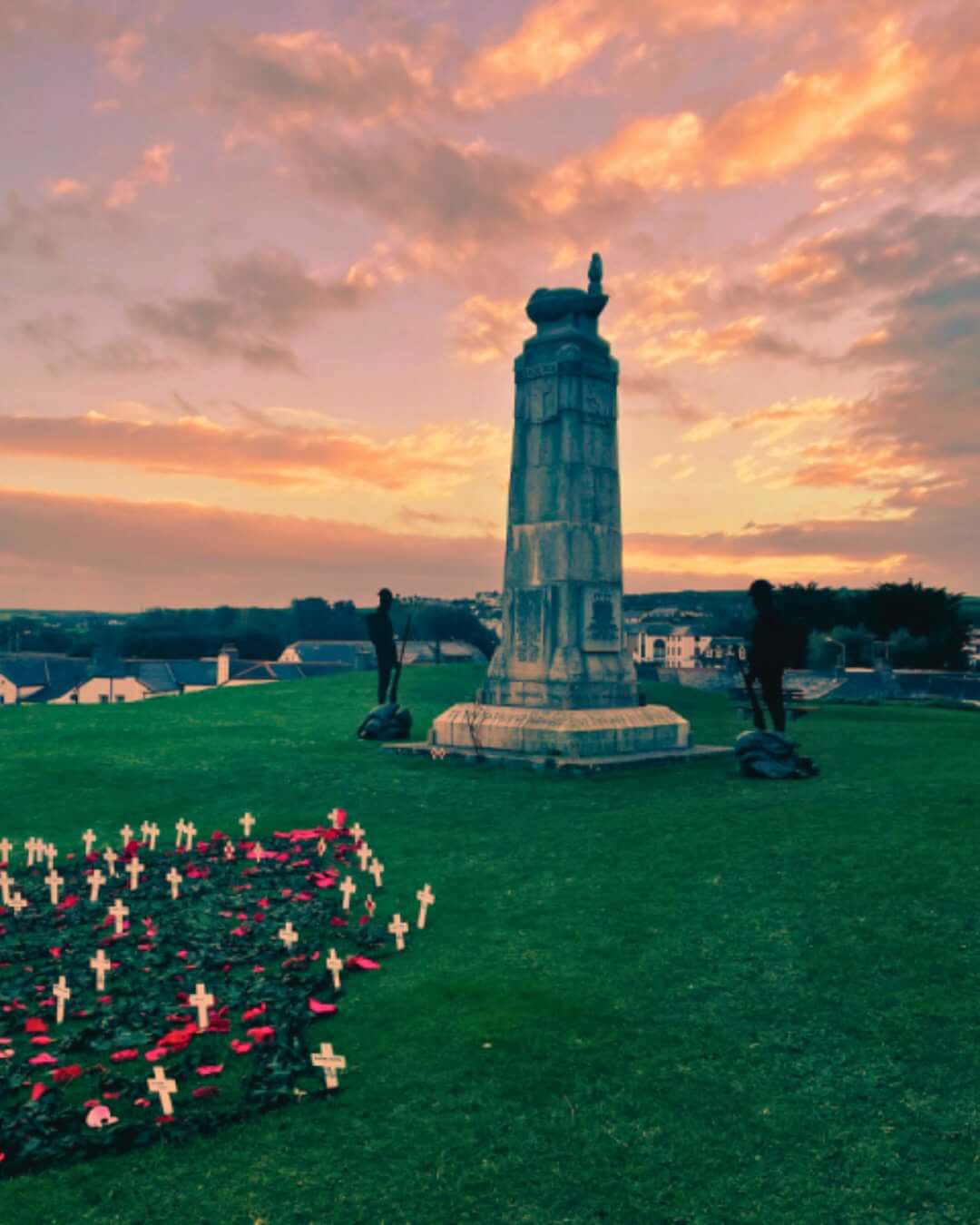 Bude War Memorial on Shalder Hill at sunset, with crosses and poppies on the grass