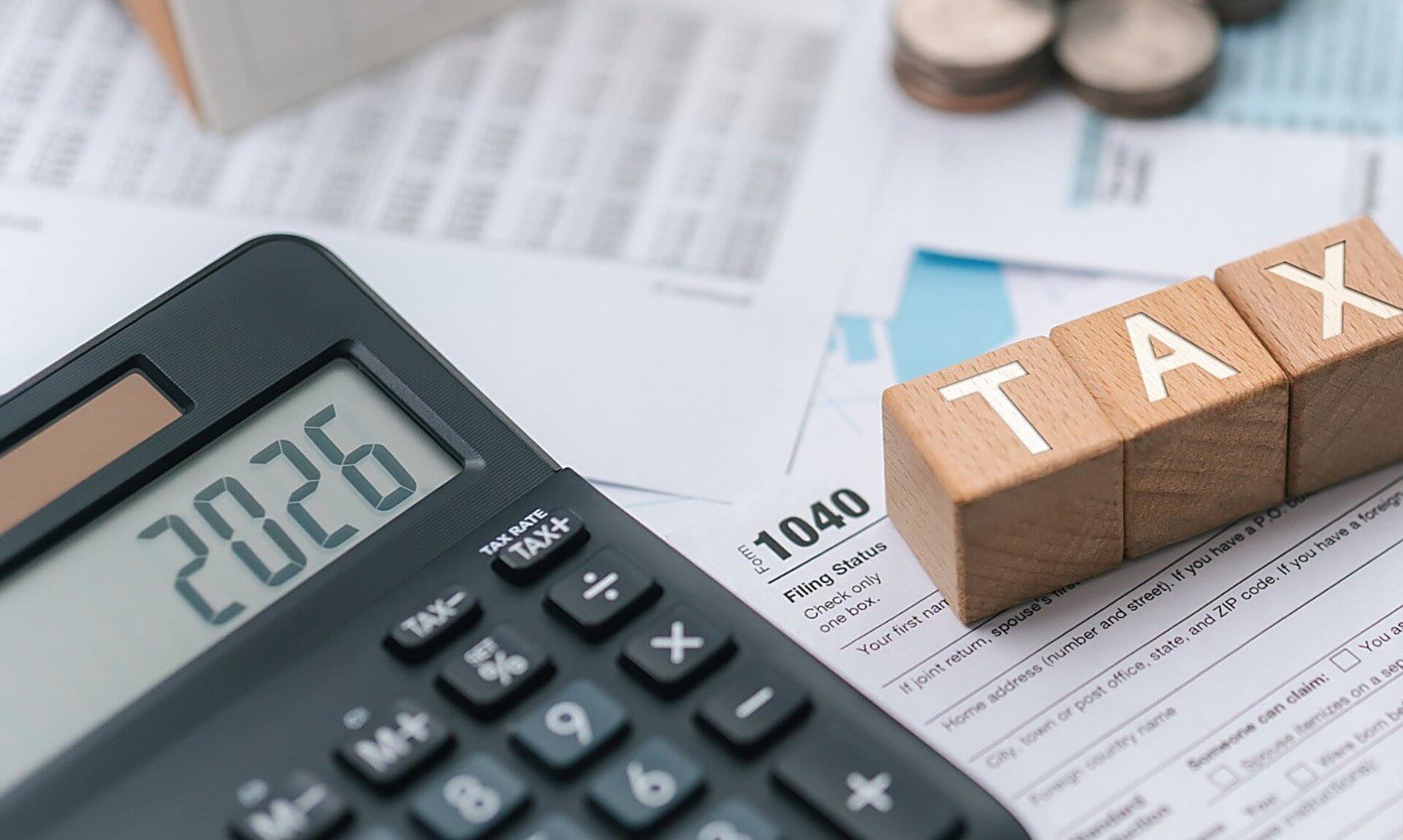 Wooden blocks spelling TAX beside a calculator showing 2026