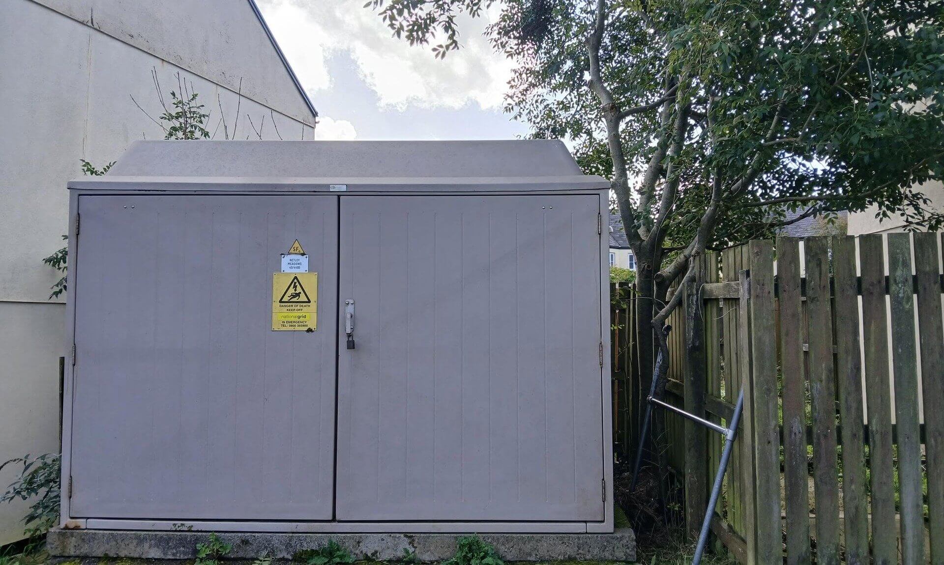 Electricity substation with a fibreglass roof beside a house and fence
