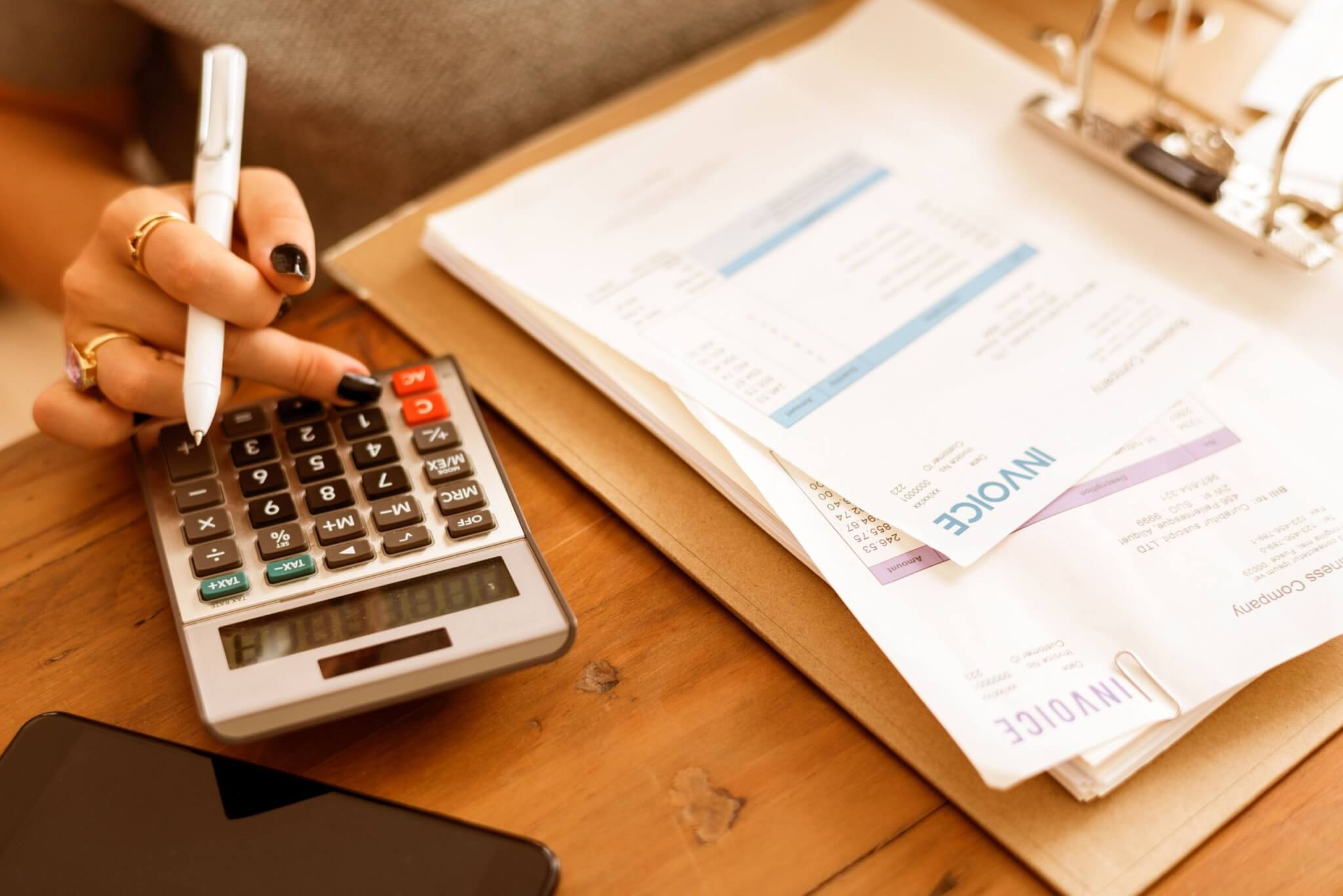 A hand using a calculator beside a folder of invoices