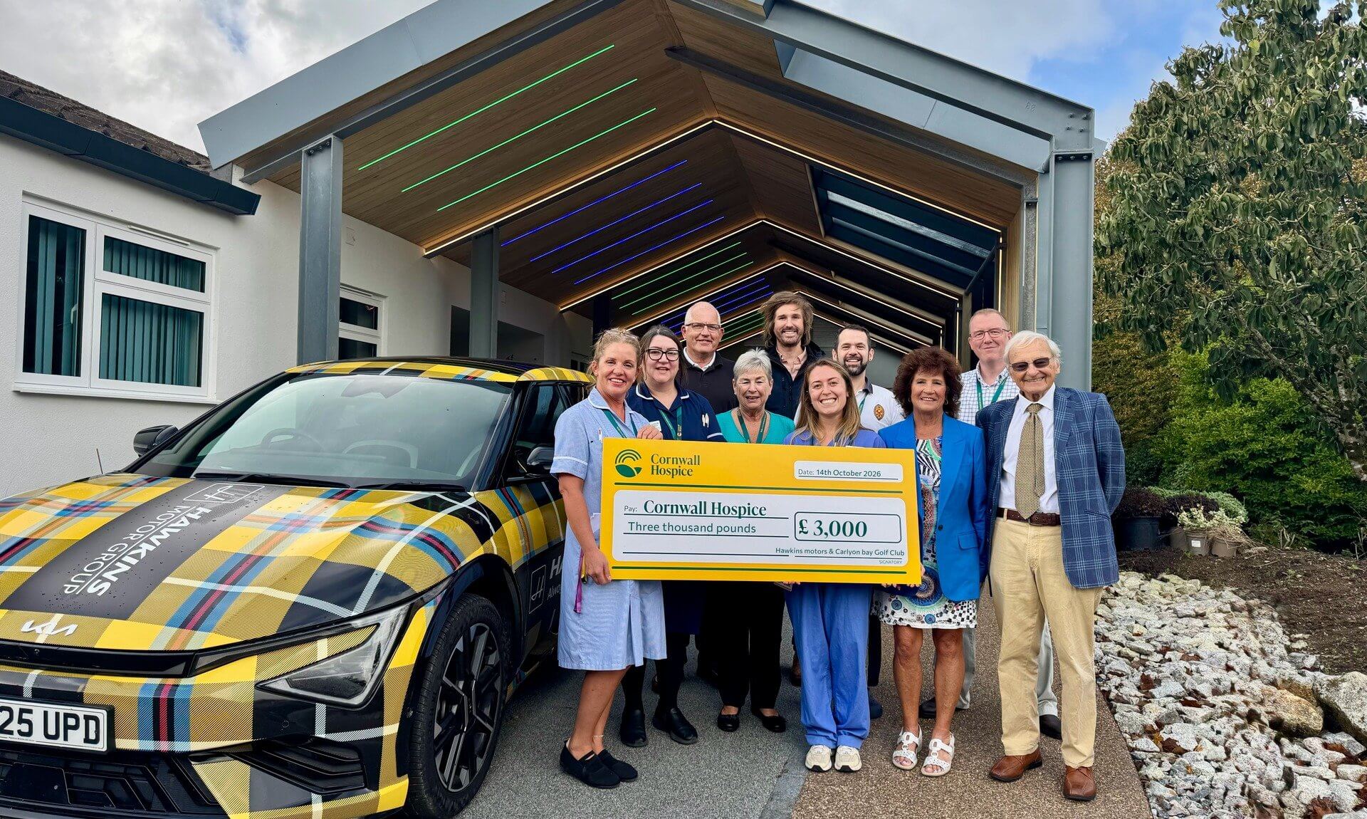 Cheque for £3,000 presented to Cornwall Hospice beside the Hawkins Motor Group tartan Kia EV6