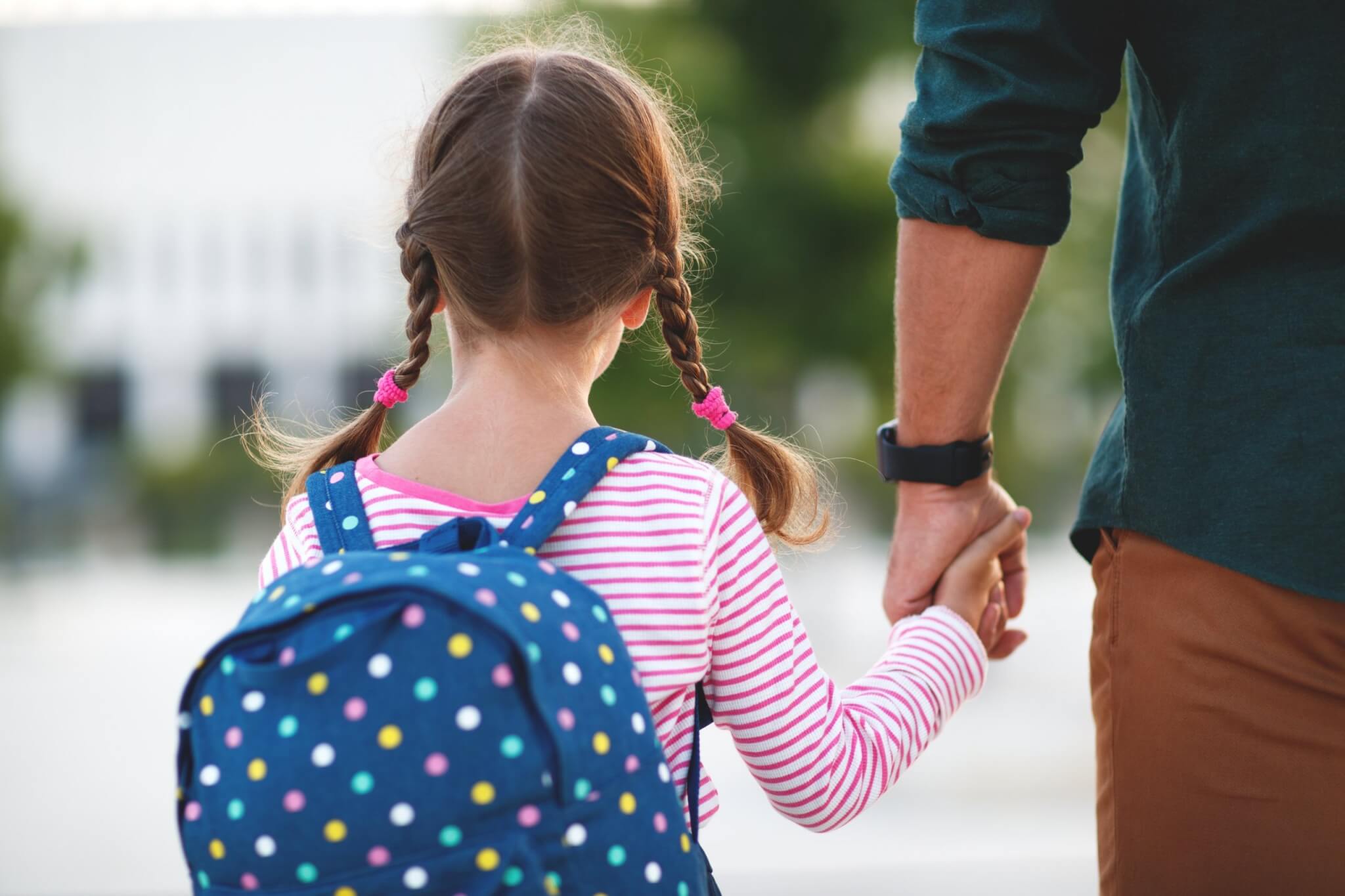 A young girl with a school backpack holding a parent's hand