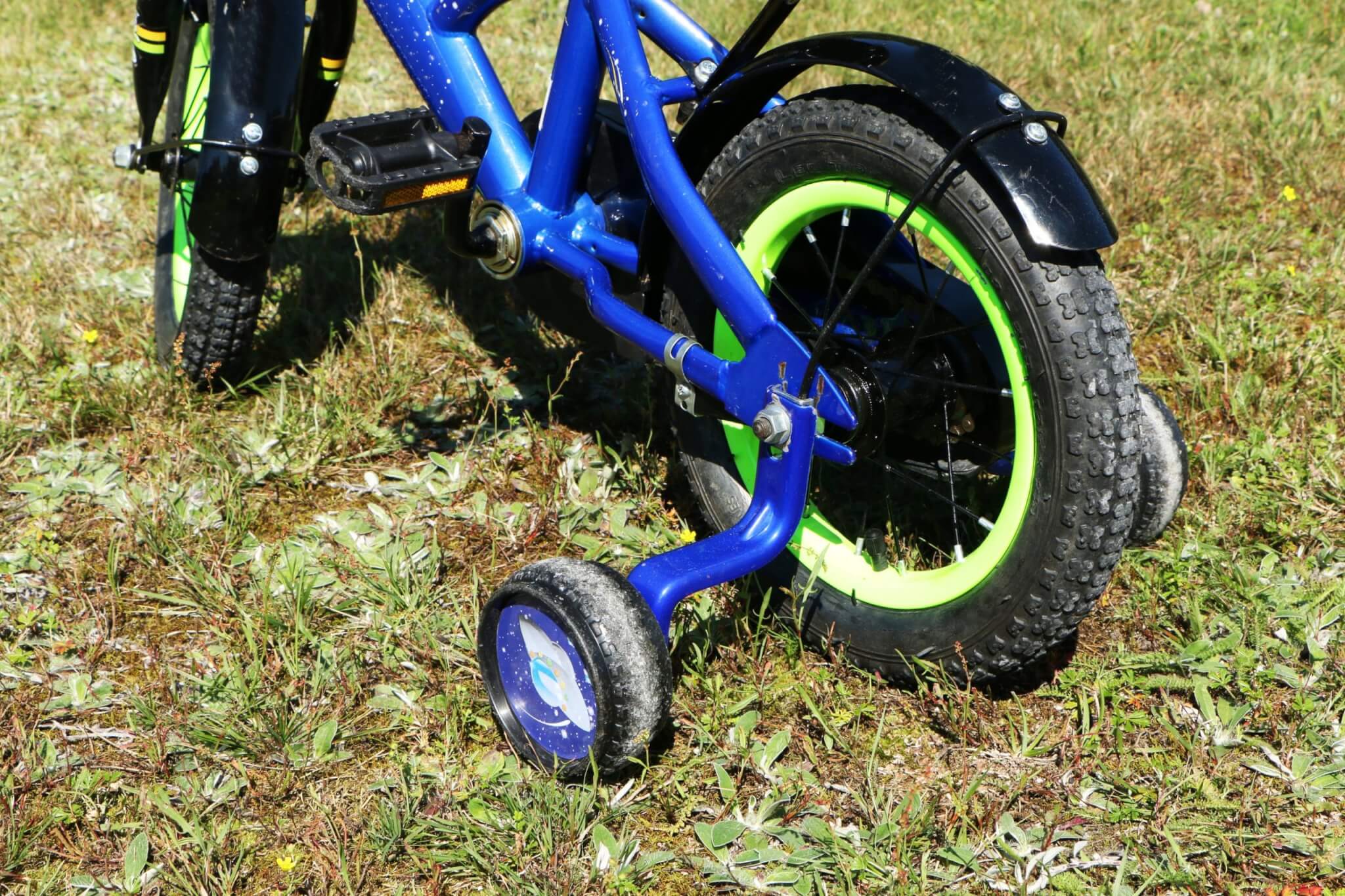 Child's blue bike with green wheels and stabilisers on grass