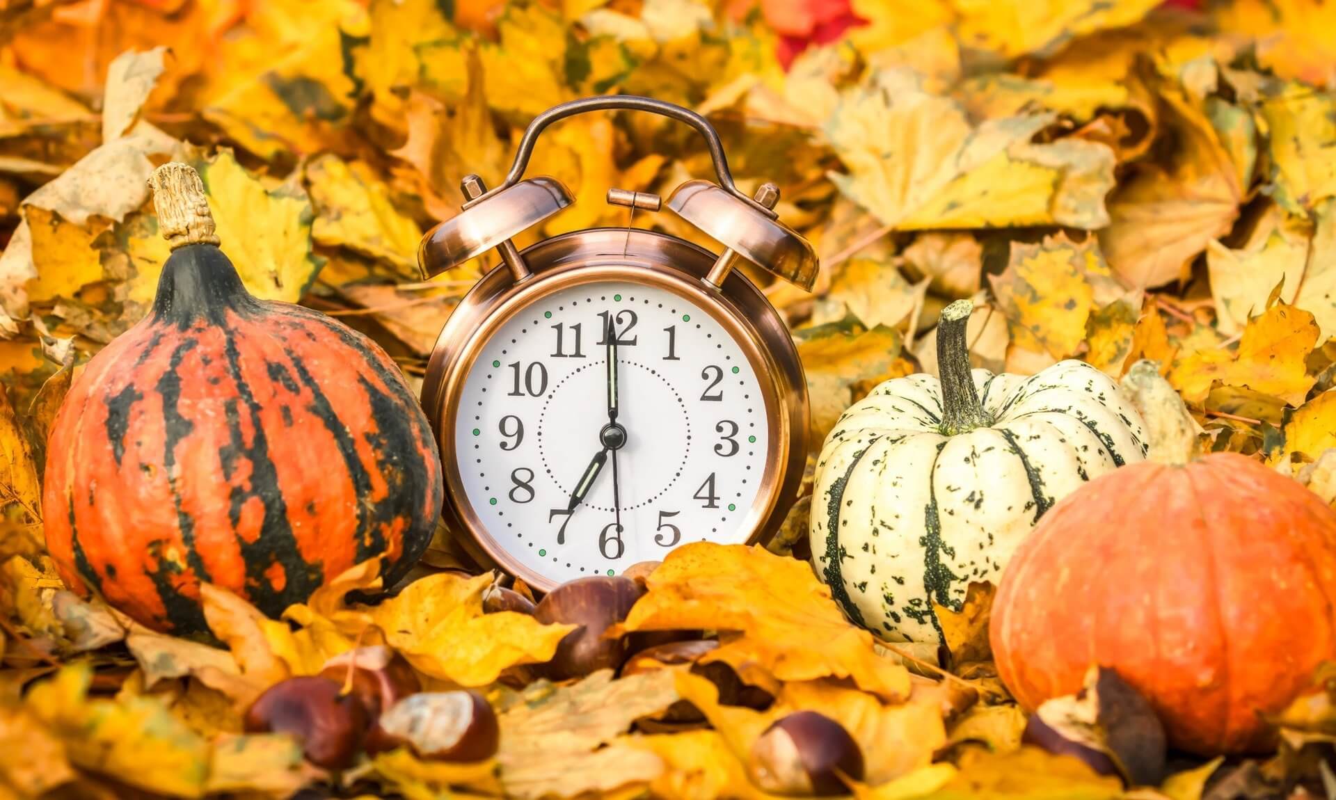 Vintage alarm clock among autumn leaves and pumpkins