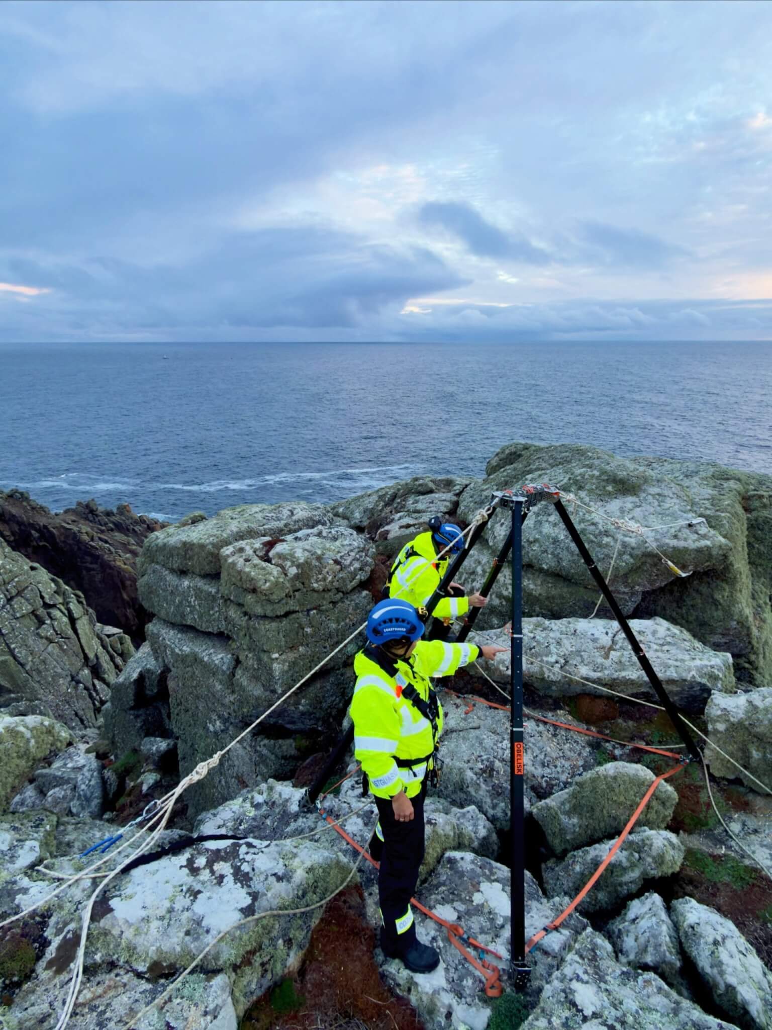 Coastguard technicians setting up a vertical rescue tripod on rocks above the sea