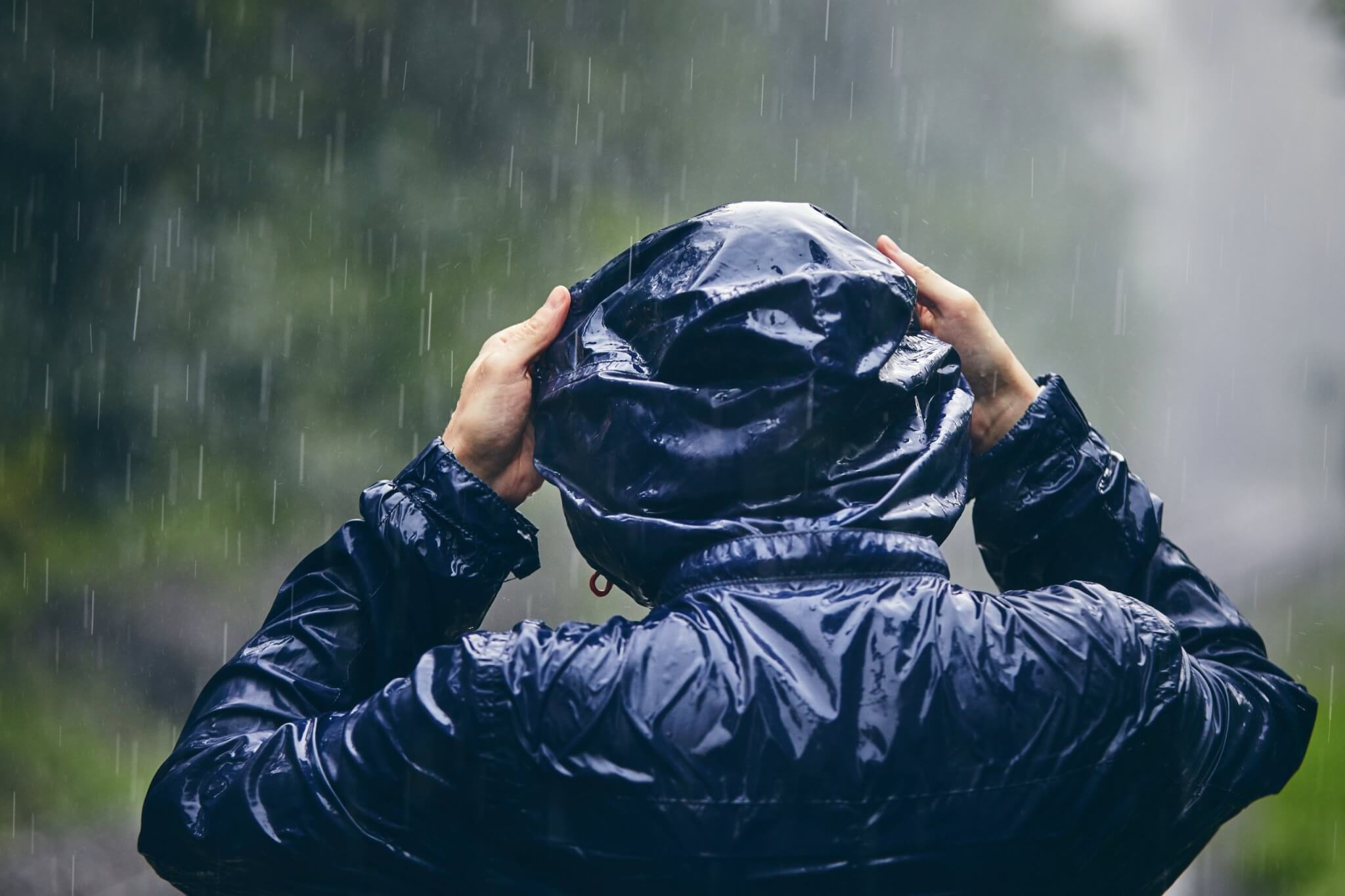 Person in a waterproof jacket pulling up their hood in heavy rain