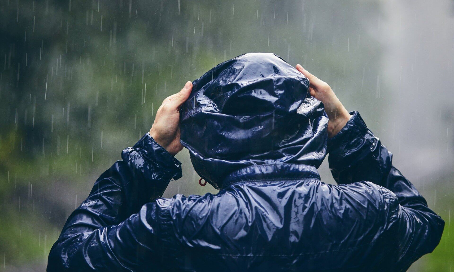 Person in a waterproof jacket pulling up their hood in heavy rain