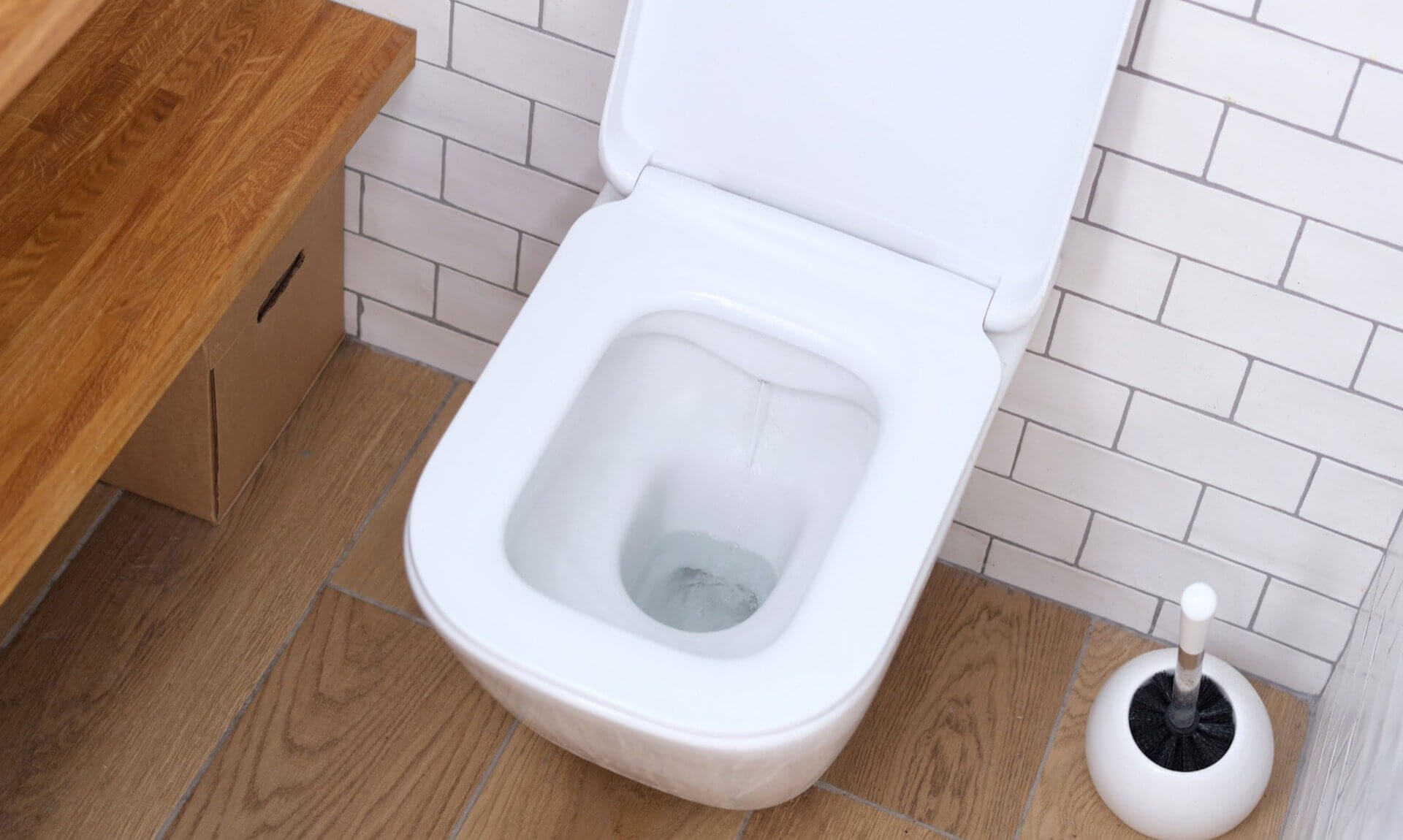 A white wall-hung toilet with the seat raised and water running into the pan