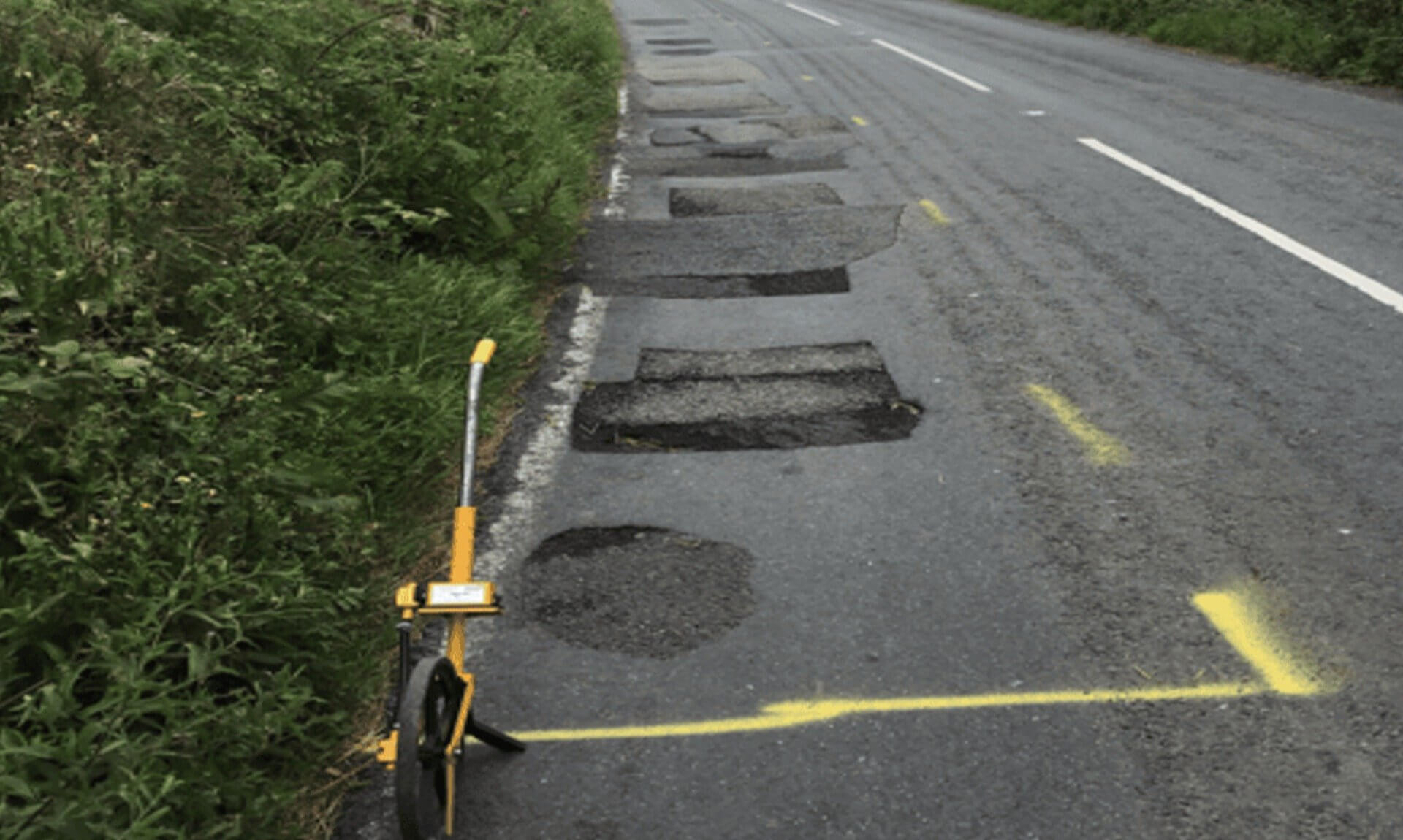 Patched road edge near Penzance with yellow repair markings and a measuring wheel
