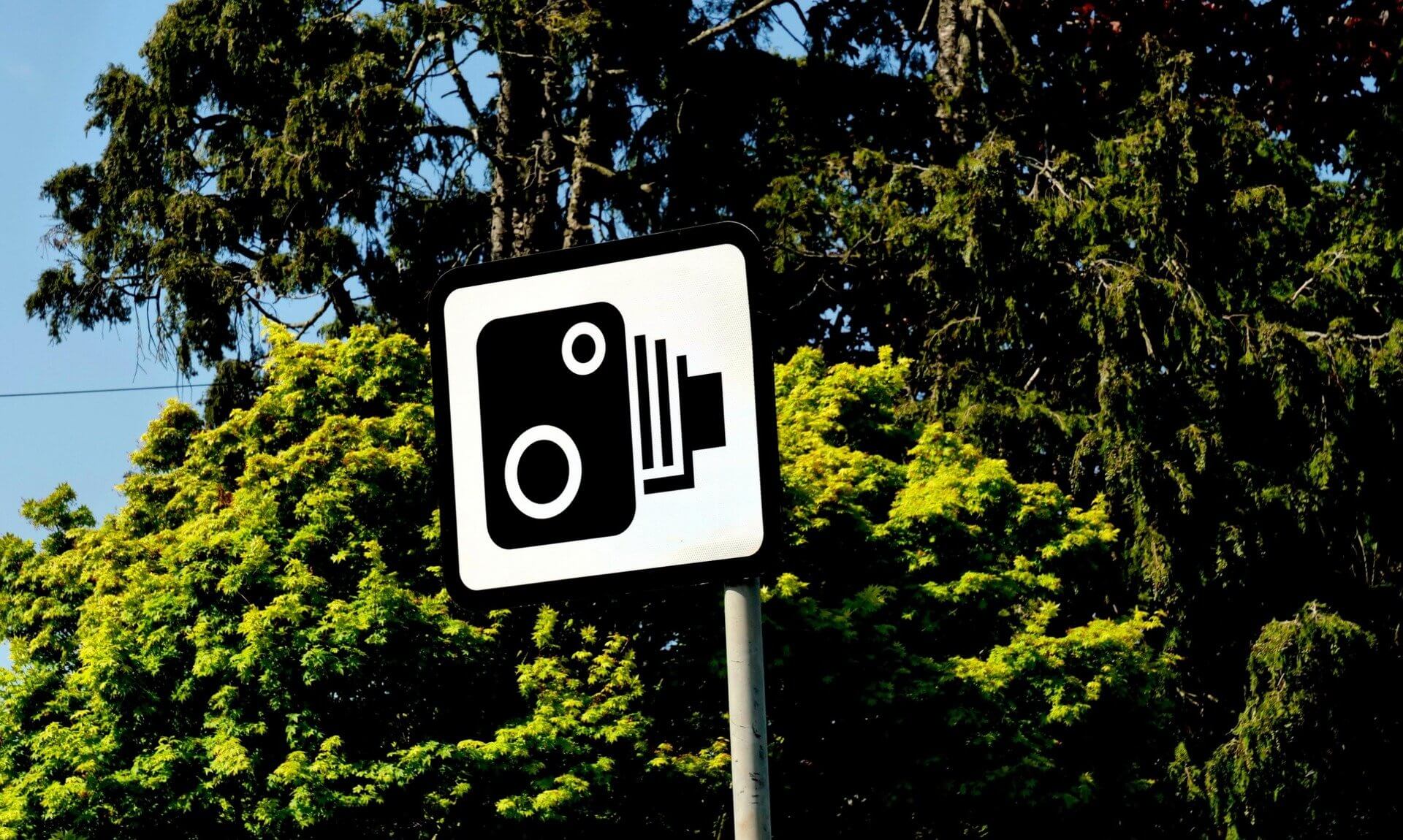 Speed camera warning sign in front of trees