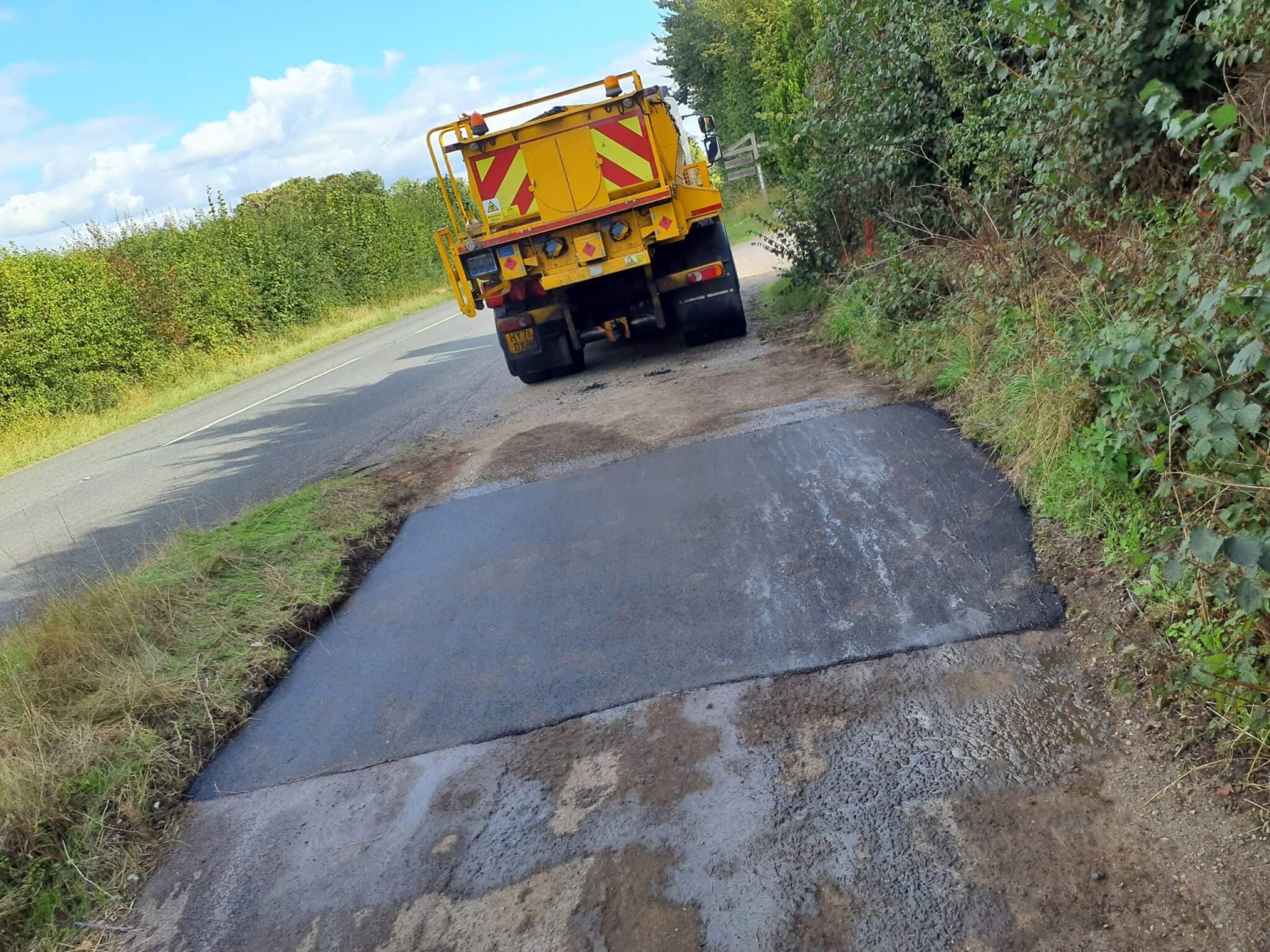 A freshly laid road patch with a highways vehicle beyond