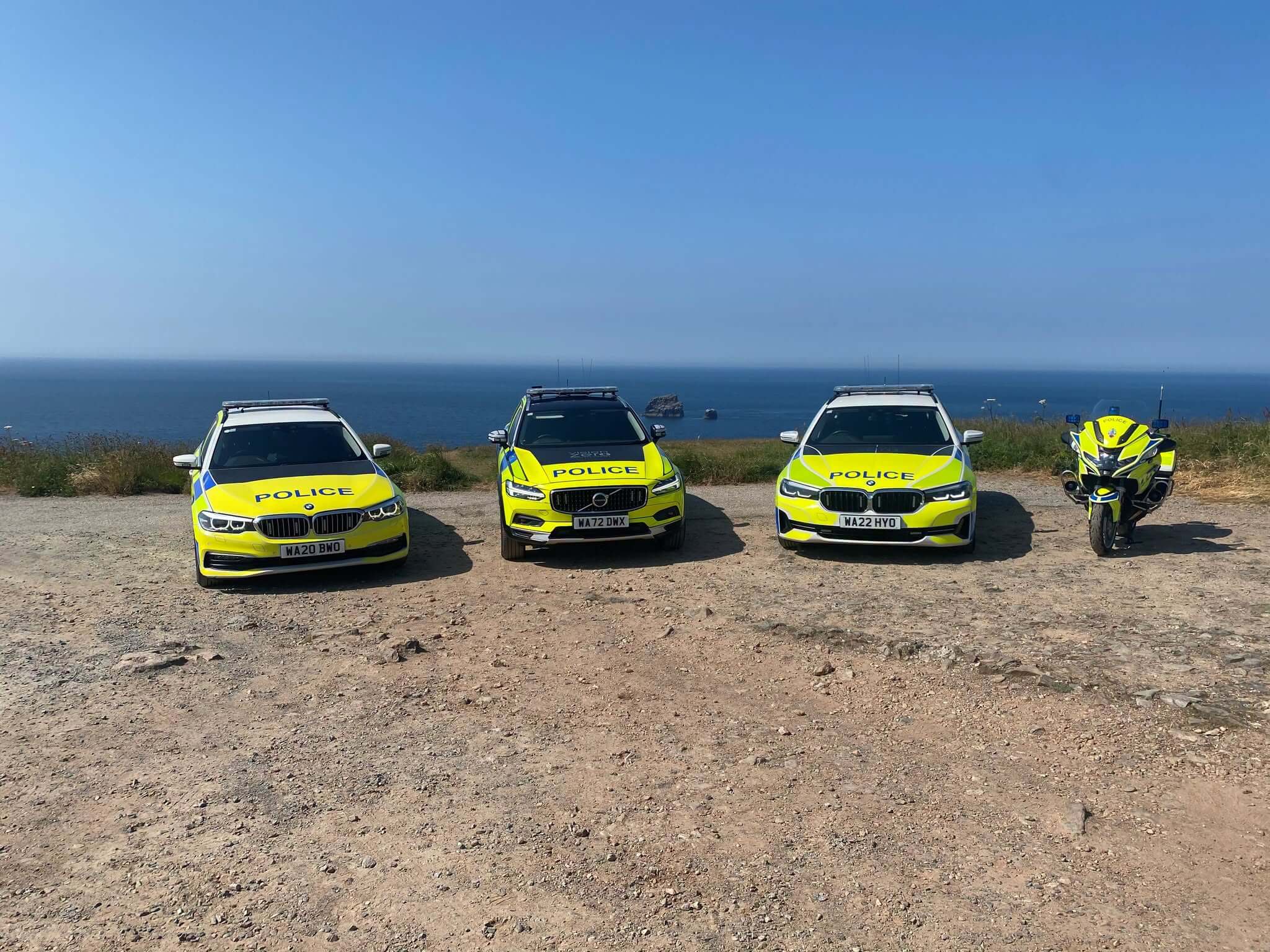 Three police cars and a police motorbike parked on a clifftop