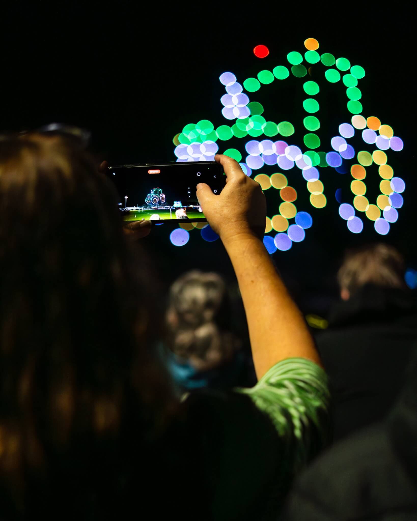 Spectator filming a drone formation on a phone