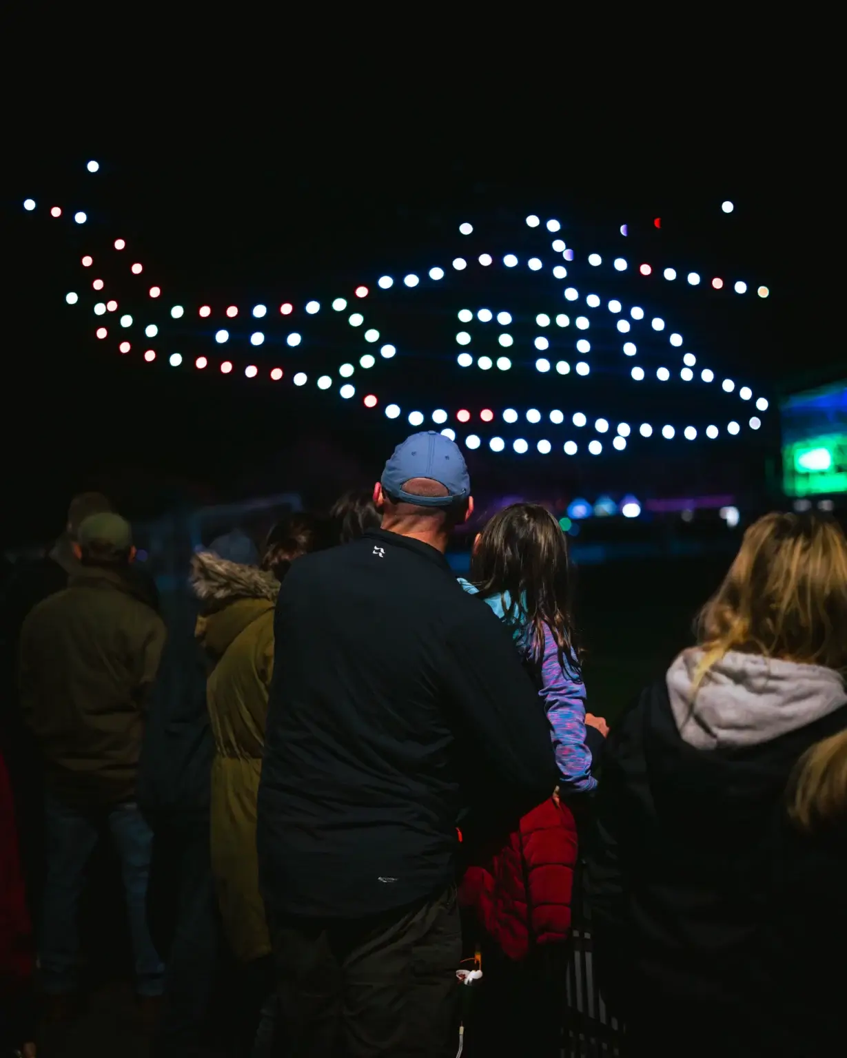 Drones forming a white helicopter shape above a watching crowd