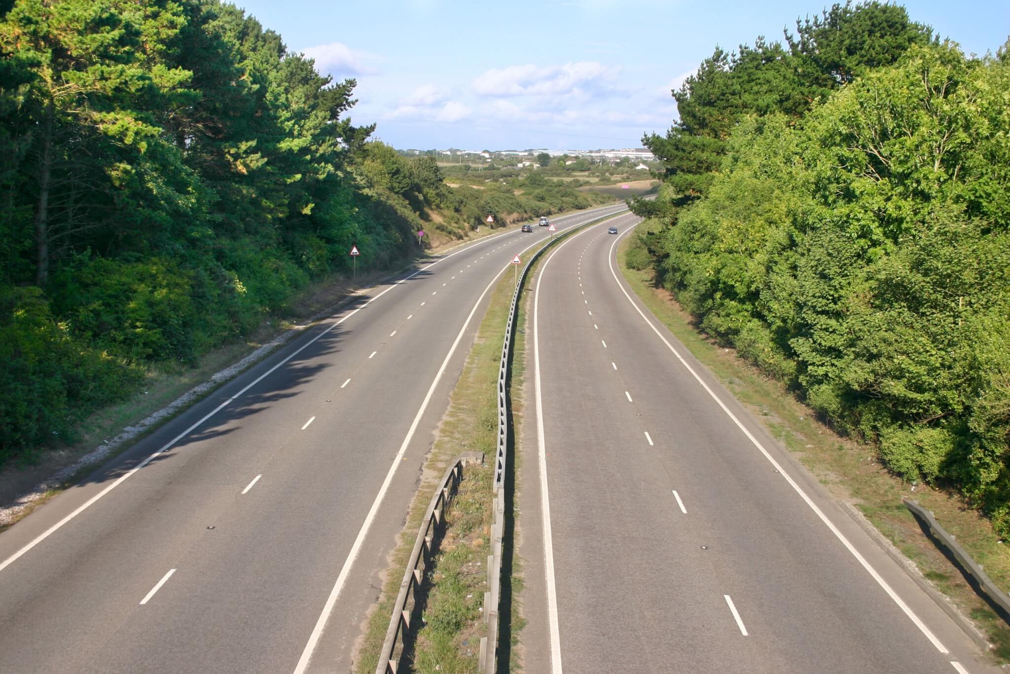 A dual carriageway seen from a bridge, with trees on both sides
