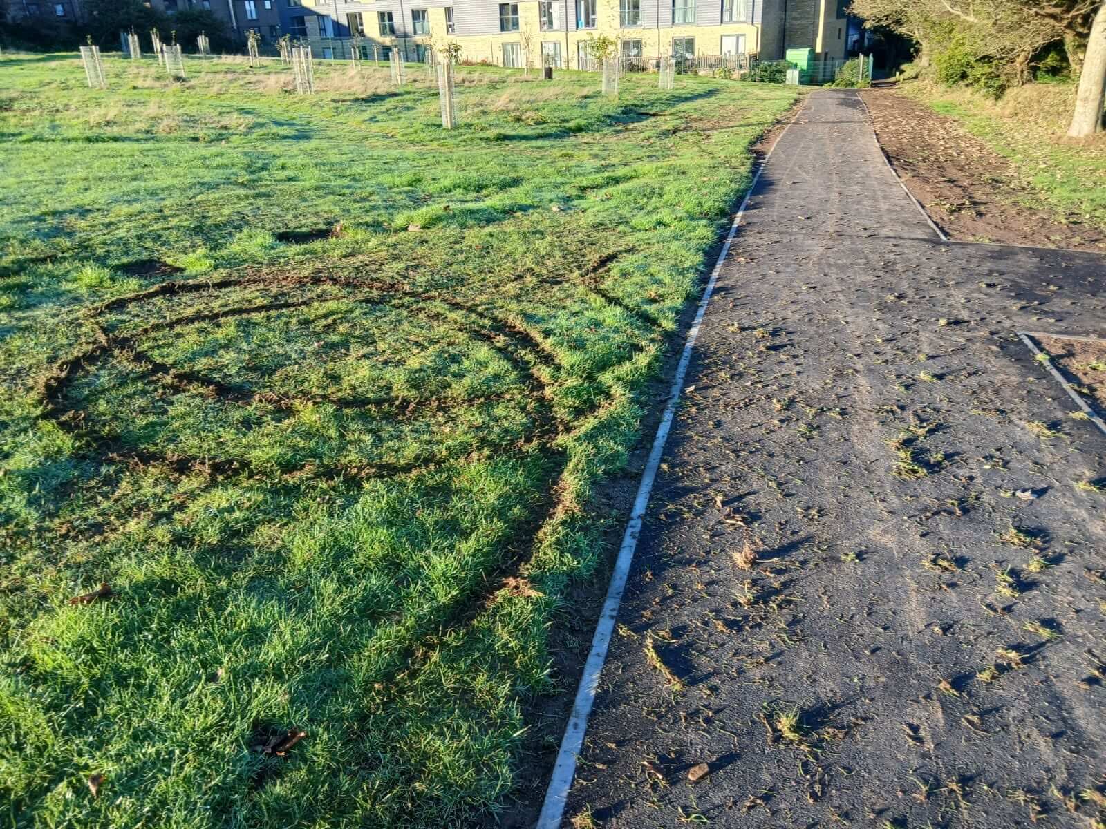 Tyre tracks cut into the grass beside a new pathway at East End Park in Redruth