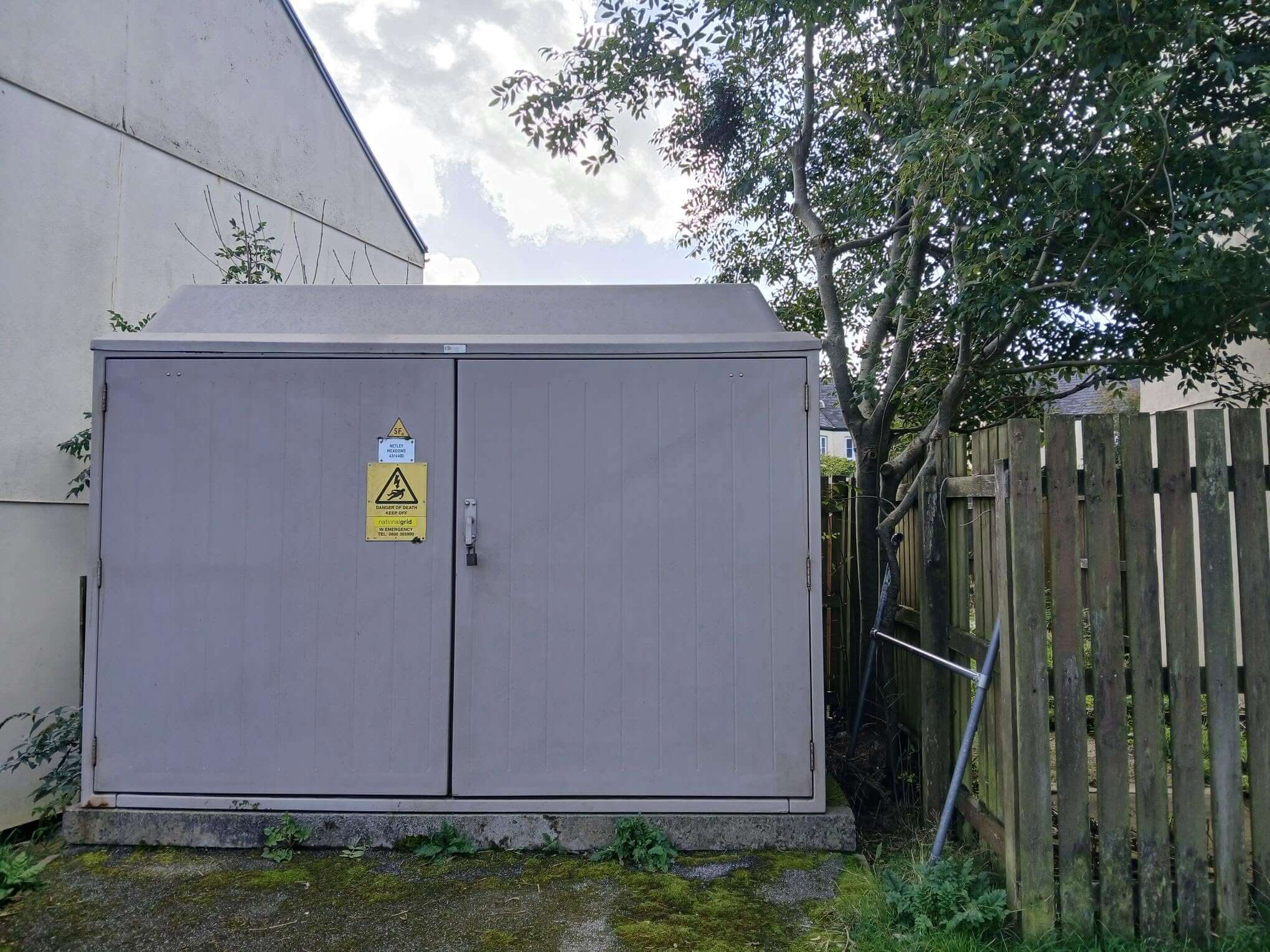 Electricity substation with a fibreglass roof beside a house and fence