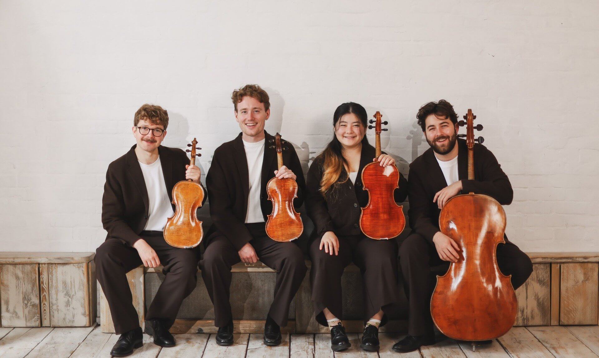The Elmore Quartet sitting on a bench holding their violins, viola and cello