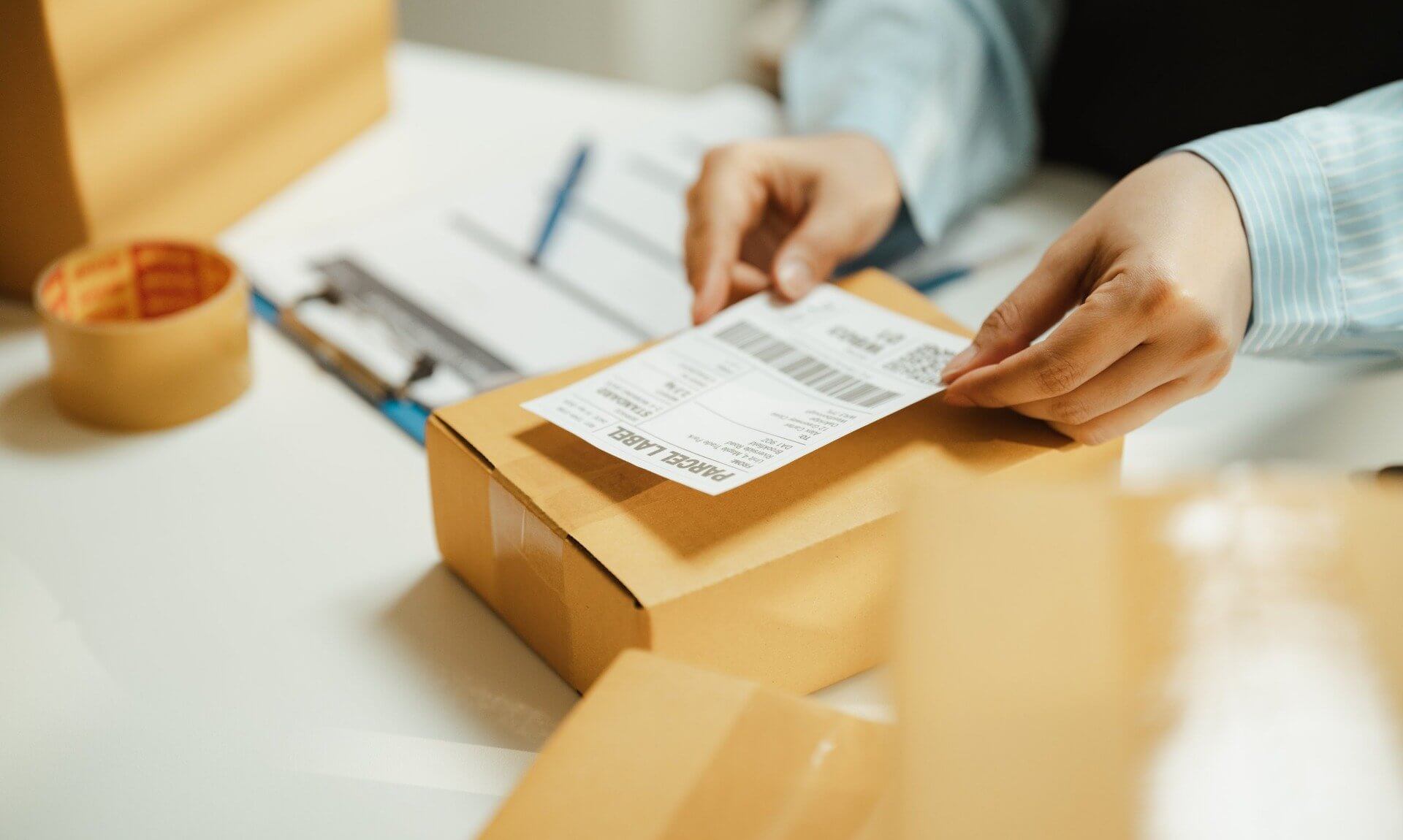 Hands attaching a parcel label to a cardboard box ready for posting