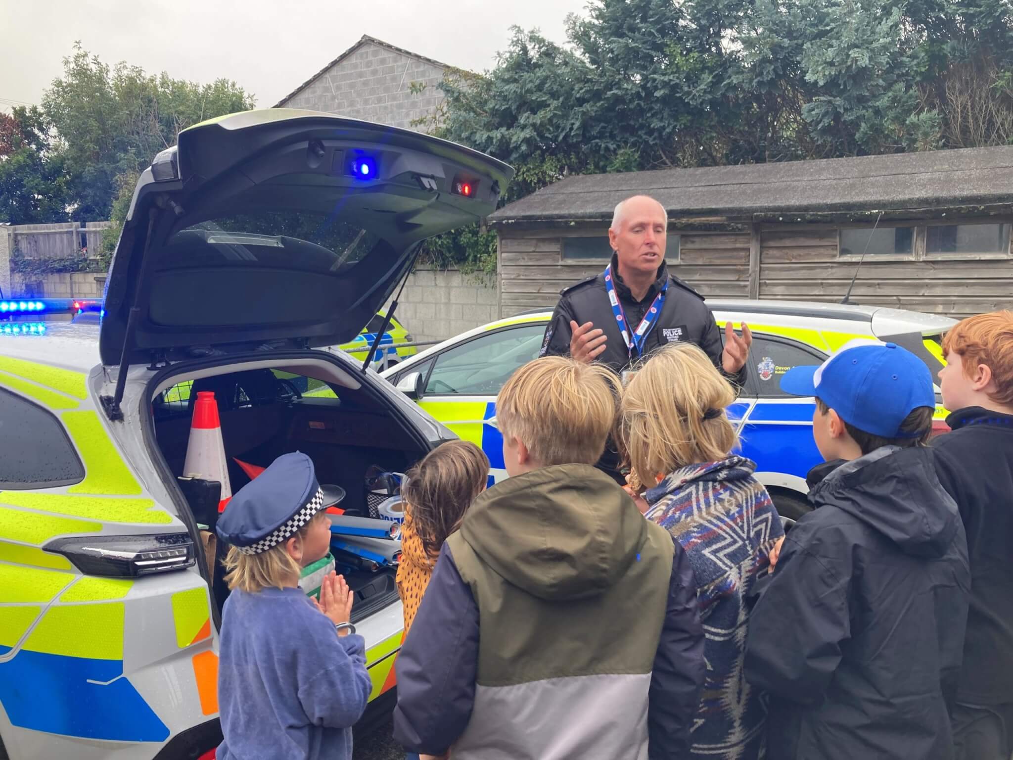 PC Colin Stirling talking to home-schooled children beside a police car at Penzance police station