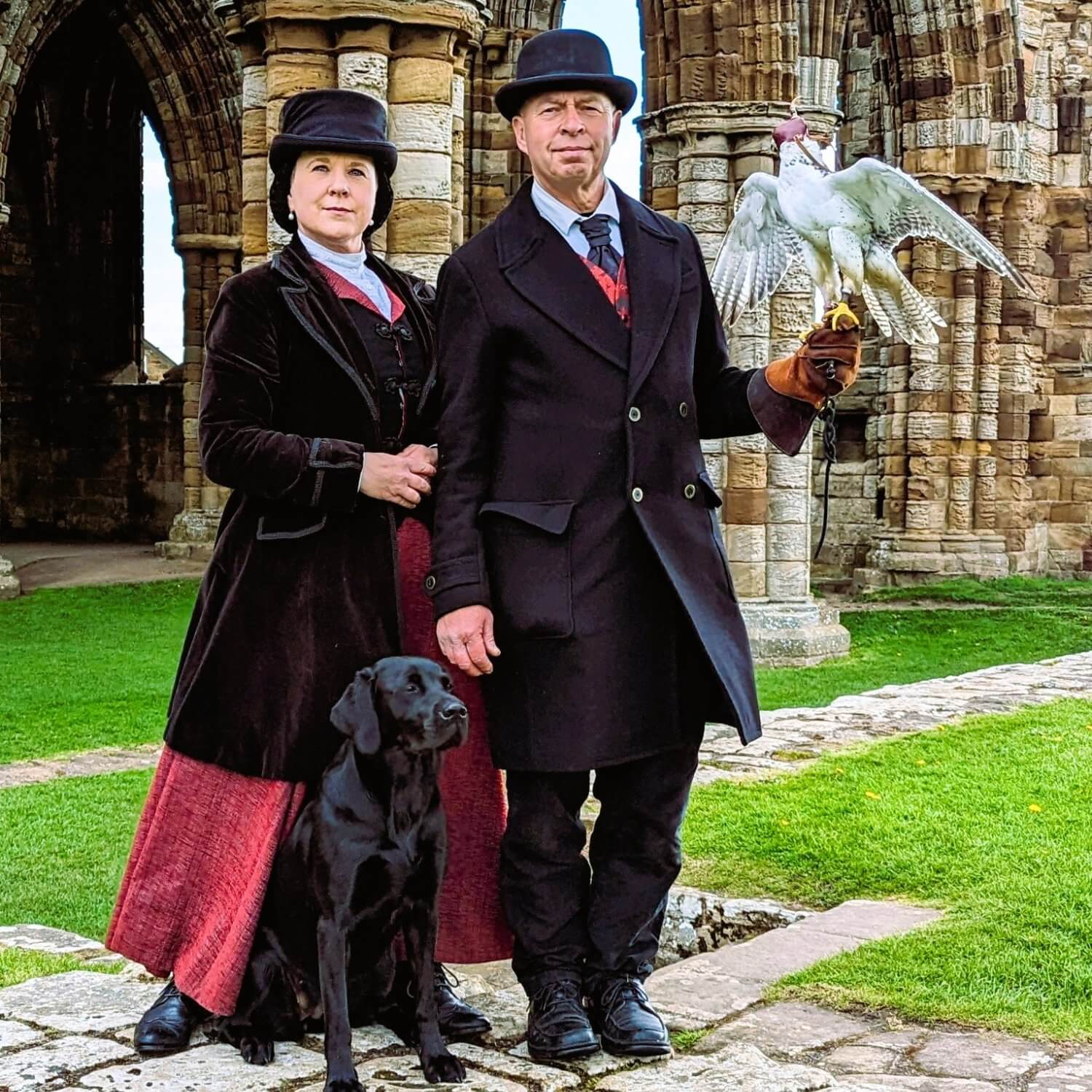 Falconers in Victorian costume with a white falcon and a black Labrador