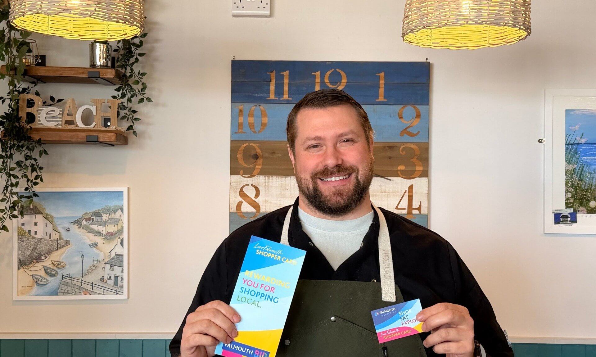 Chris at Koffiji in Falmouth holding a LoveFalmouth Shopper Card and leaflet