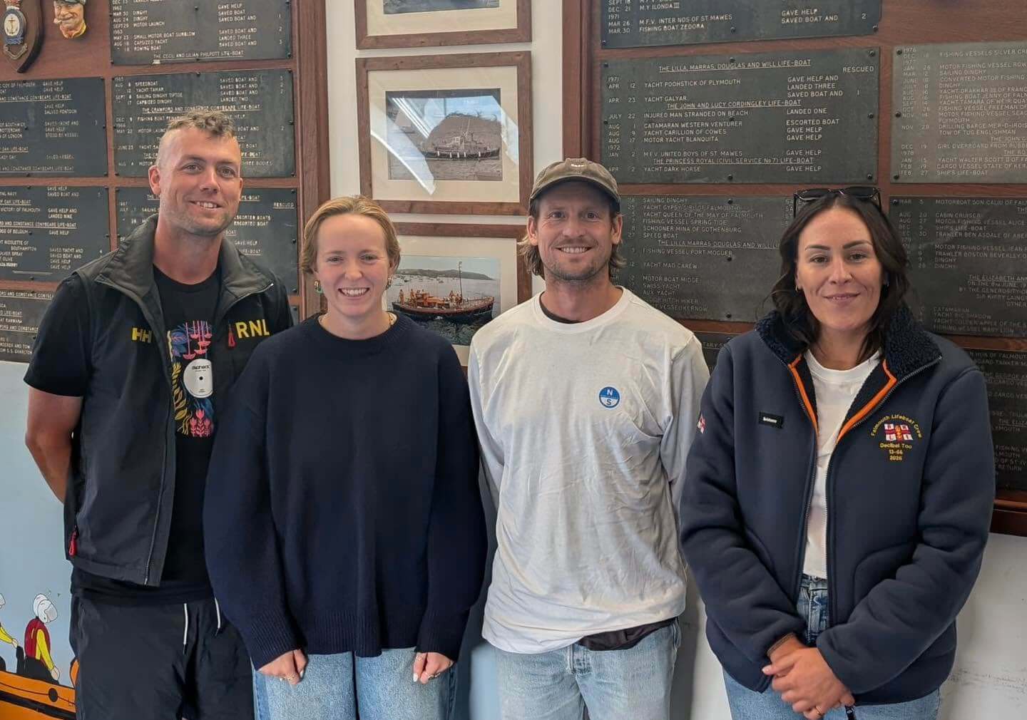 Four Falmouth Lifeboat volunteers in front of the station's service record boards