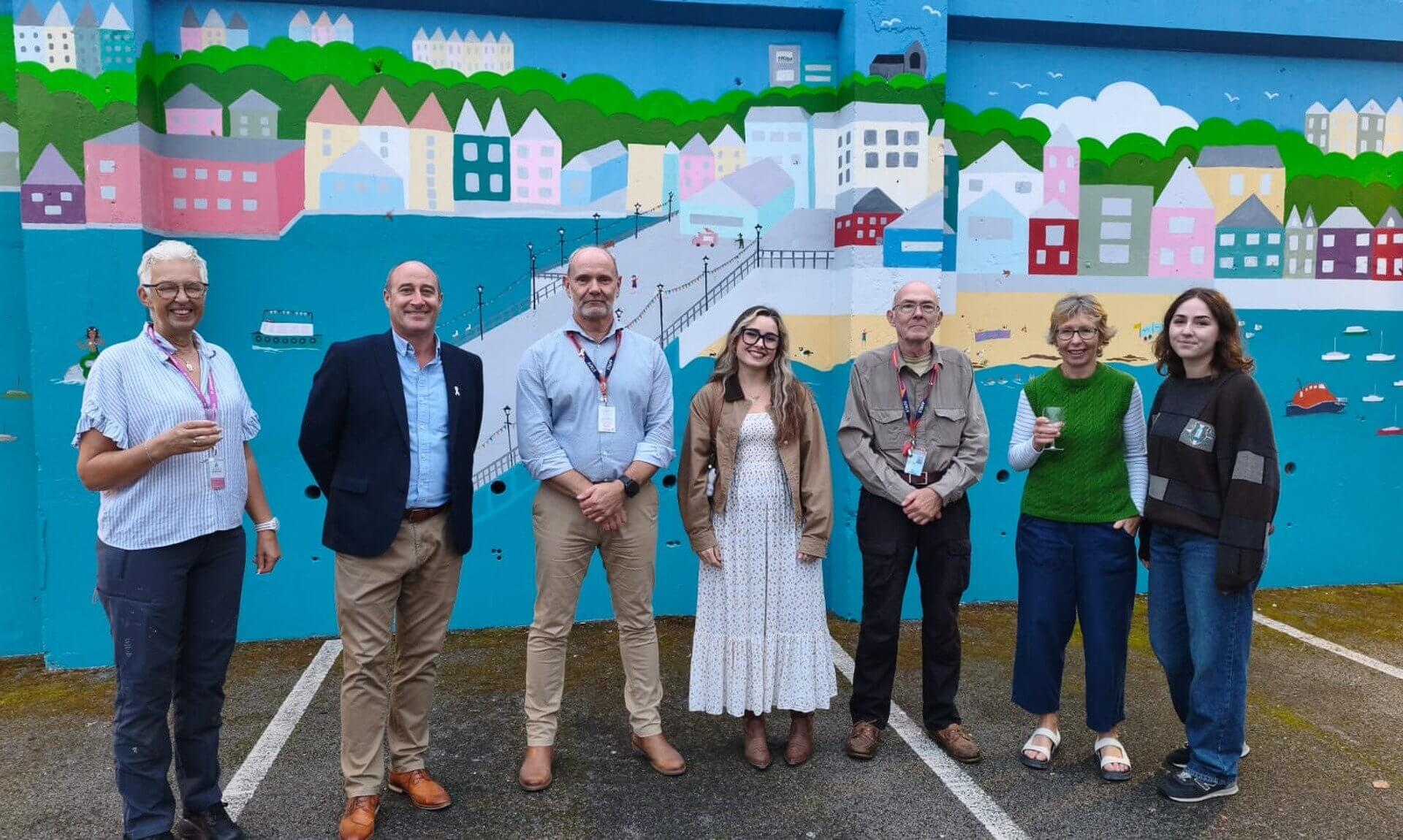 Seven people standing in front of the Falmouth mural at Falmouth Marine School