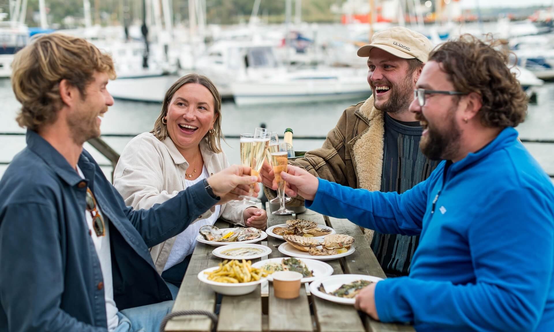 Friends raising a glass over plates of oysters by the harbour at Falmouth Oyster Festival