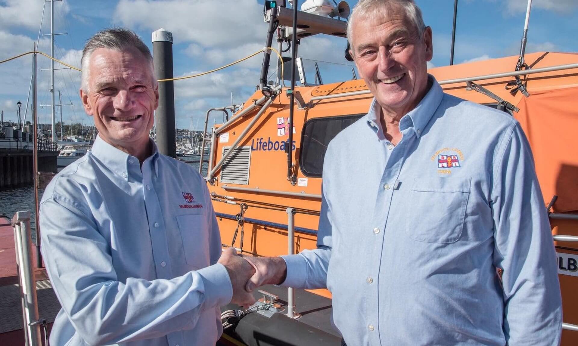 Nick Lewis and Jerry Plant shaking hands beside the Falmouth RNLI all-weather lifeboat