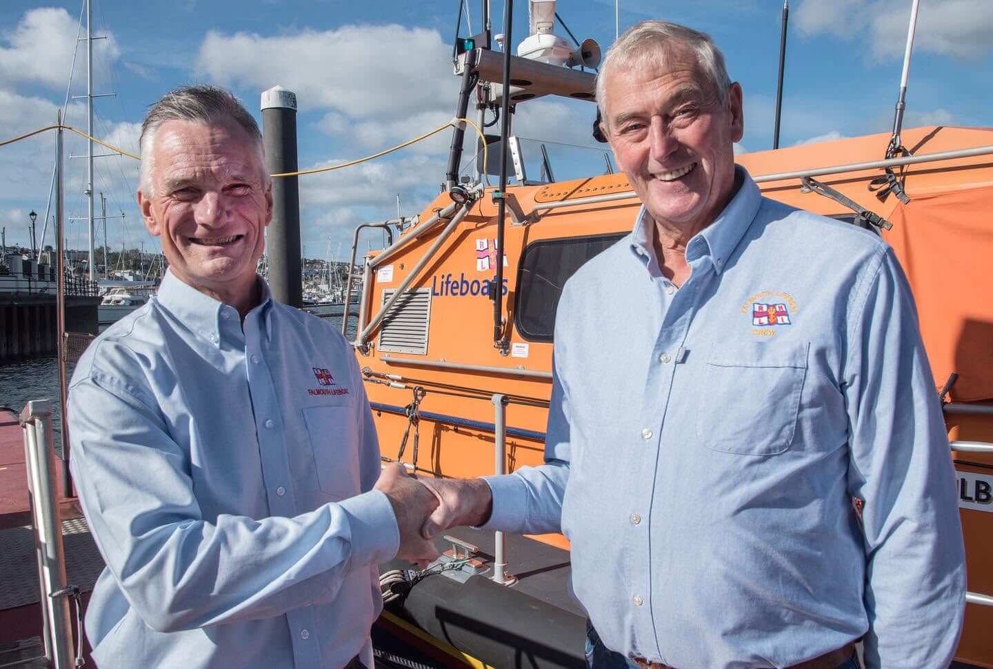 Nick Lewis and Jerry Plant shaking hands beside the Falmouth RNLI all-weather lifeboat