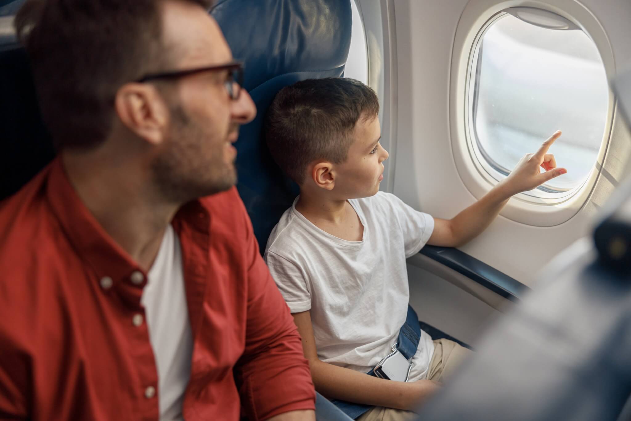 A father and his young son sitting together on a plane, the boy pointing out of the window