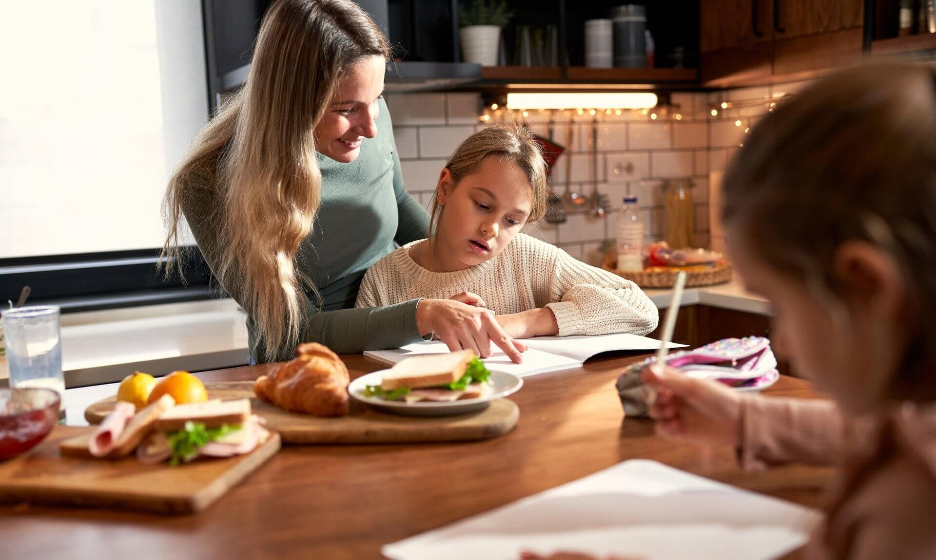 Woman helping a girl with homework at a kitchen table