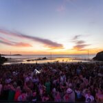 Crowds on the sand at Lusty Glaze, Newquay, as the sun sets over the Atlantic