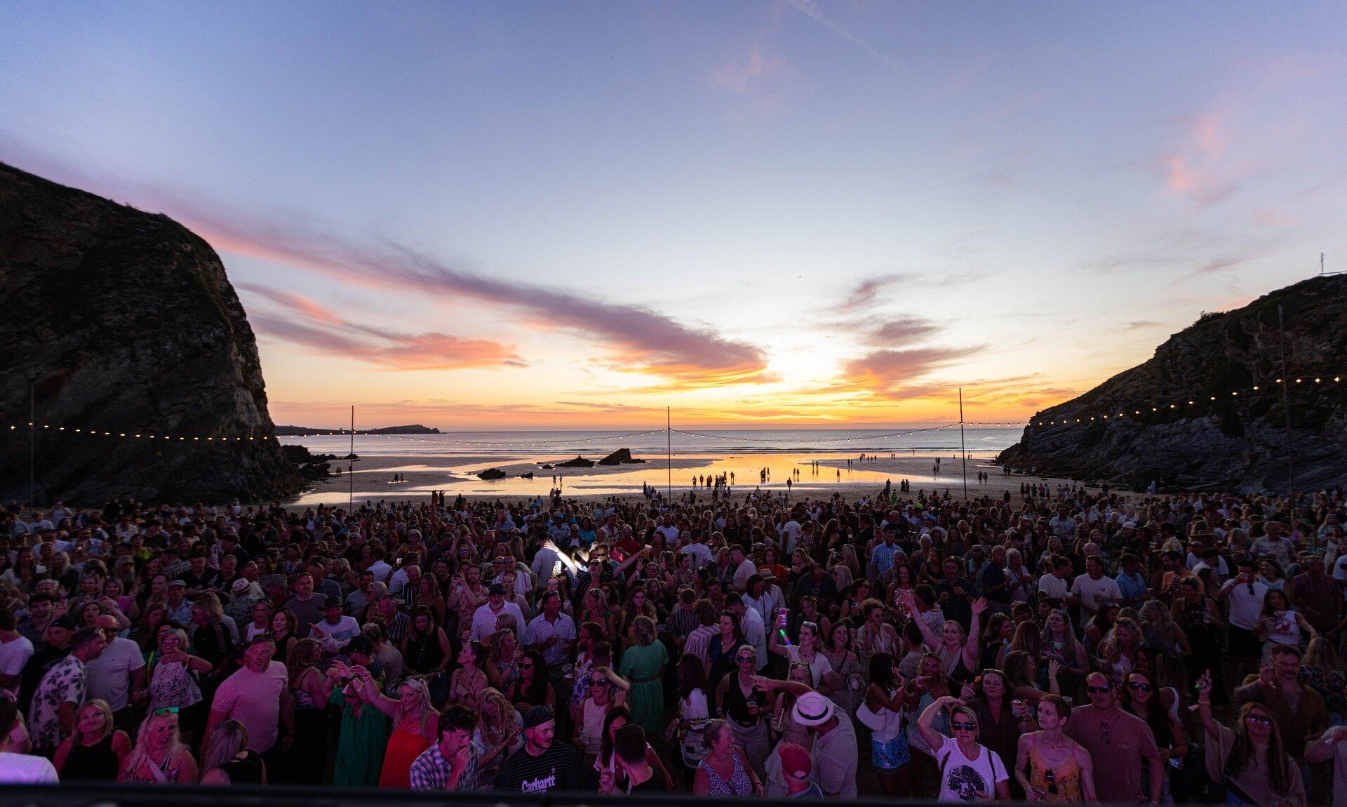 Crowds on the sand at Lusty Glaze, Newquay, as the sun sets over the Atlantic