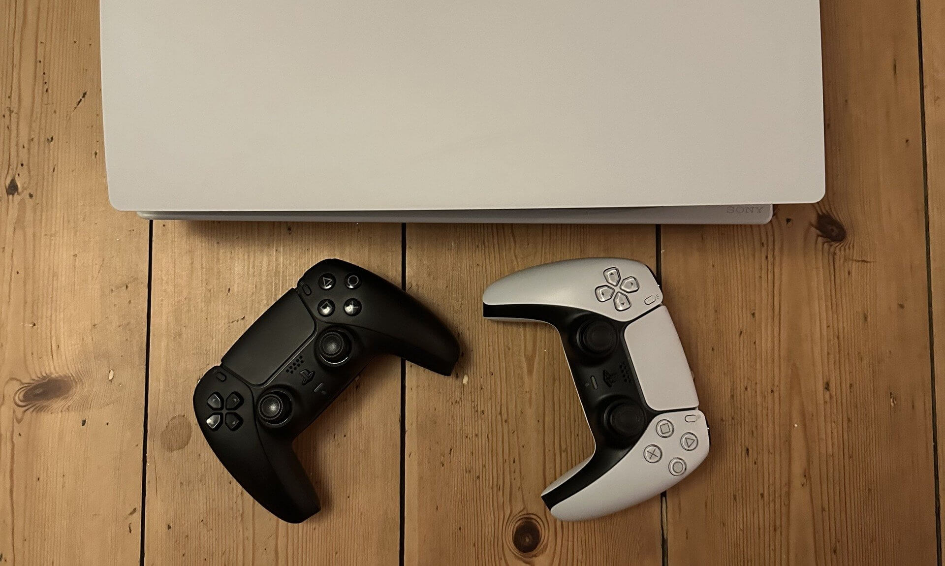 A games console and two controllers on a wooden floor